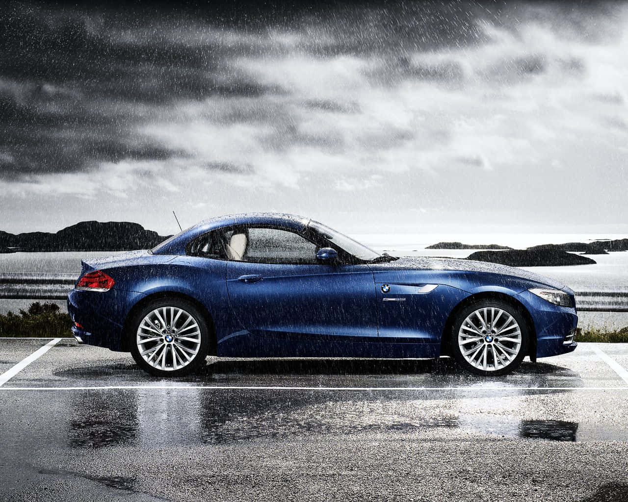 Bmw Z4 桌布 壁紙 — 一架時尚的藍色BMW Z4開篷跑車停泊在濕滑的停車場，頭頂上是戲劇性的暴風雲。