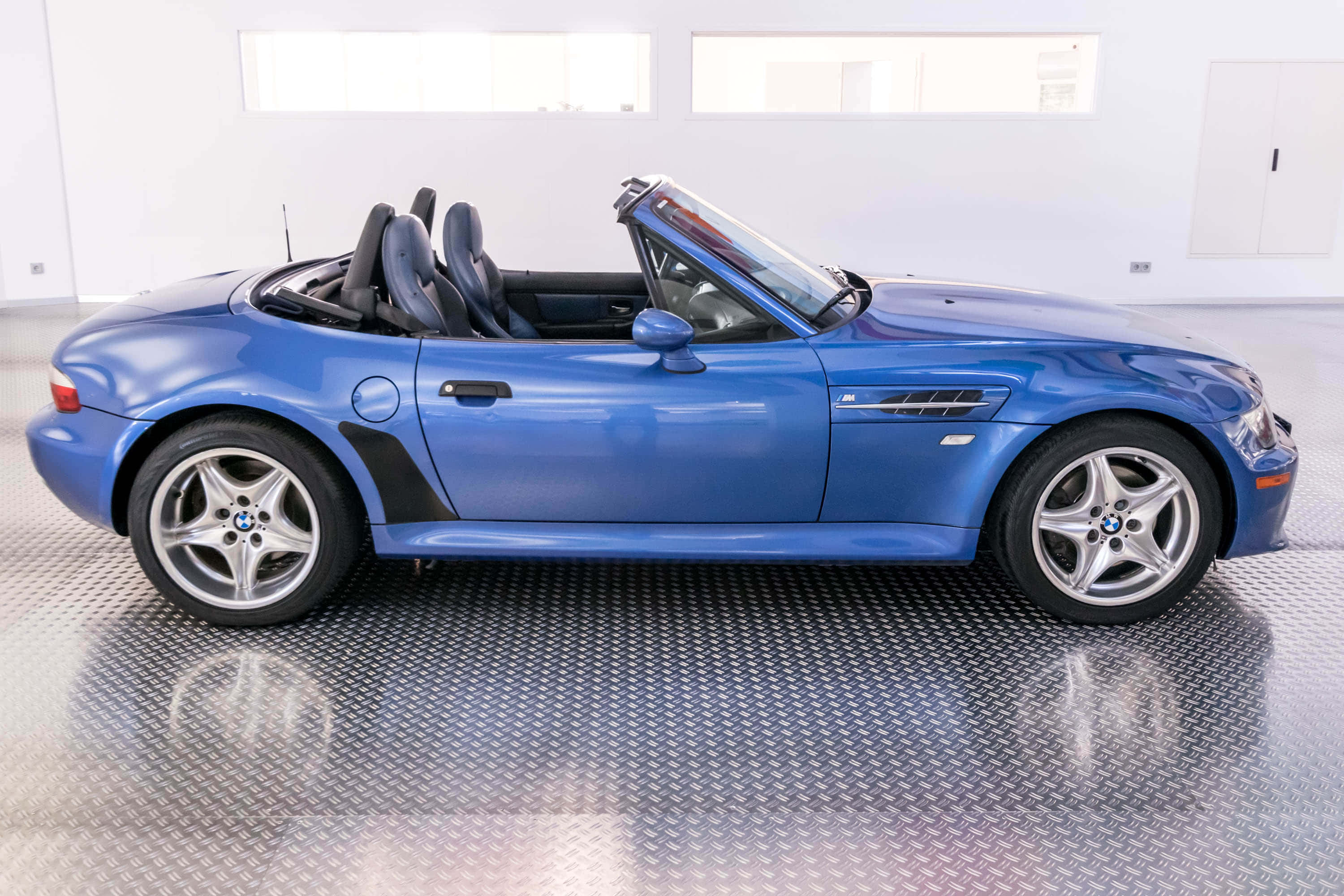 Bmw Z3 桌布 壁紙 — 一架時尚的藍色BMW Z8開篷跑車，車頂敞開，停泊在明亮白色車庫的鑽石紋地板上。