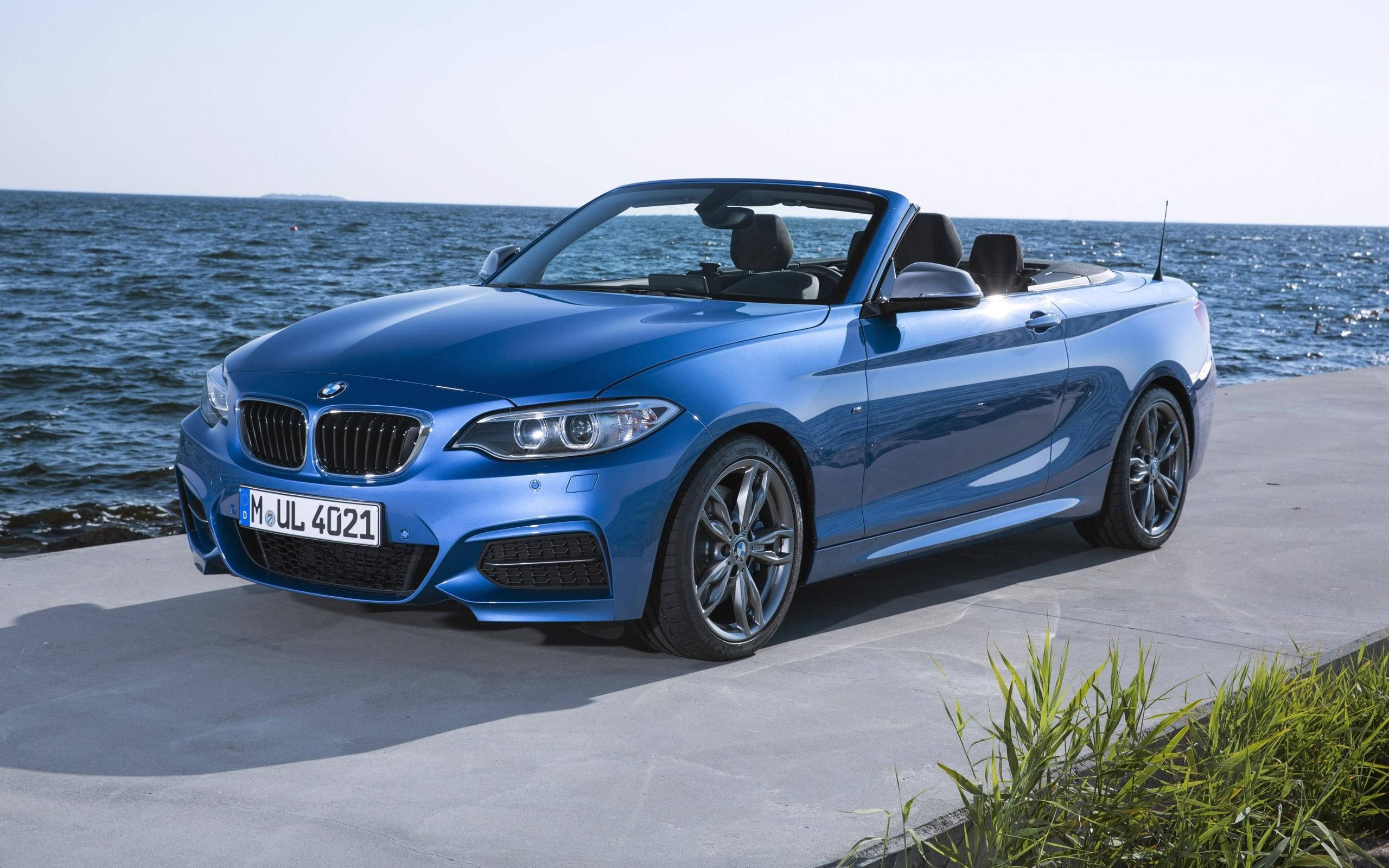 Bmw M4 桌布 壁紙 — 一架時尚的藍色BMW開篷車停在混凝土碼頭上，背後在明亮的日光下海浪拍打。