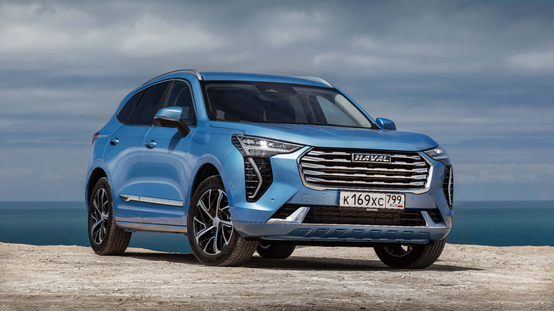 Haval 桌布 壁紙 — 一架時尚的藍色哈弗SUV停泊在岩石懸崖上，俯瞰著多雲天空下的海洋。