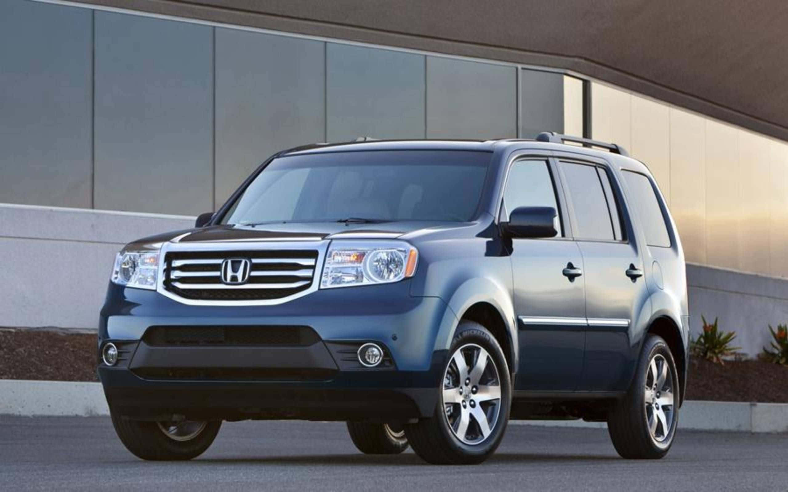 Honda Pilot 桌布 壁紙 — 一架時尚的藍色本田Pilot SUV停泊在現代玻璃建築前，溫暖的陽光投下柔和陰影。