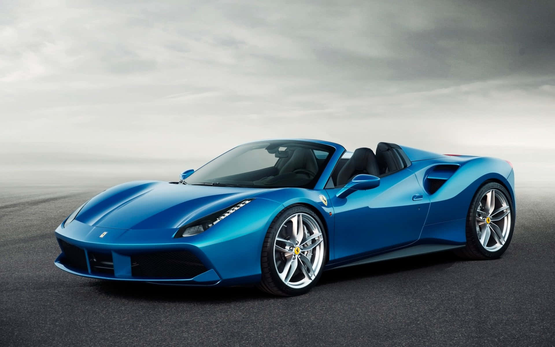Ferrari 488 Spider 桌布 壁紙 — 一架時尚的藍色法拉利開篷跑車在多雲的天空下，在霧濛濛的瀝青路上閃閃發光。