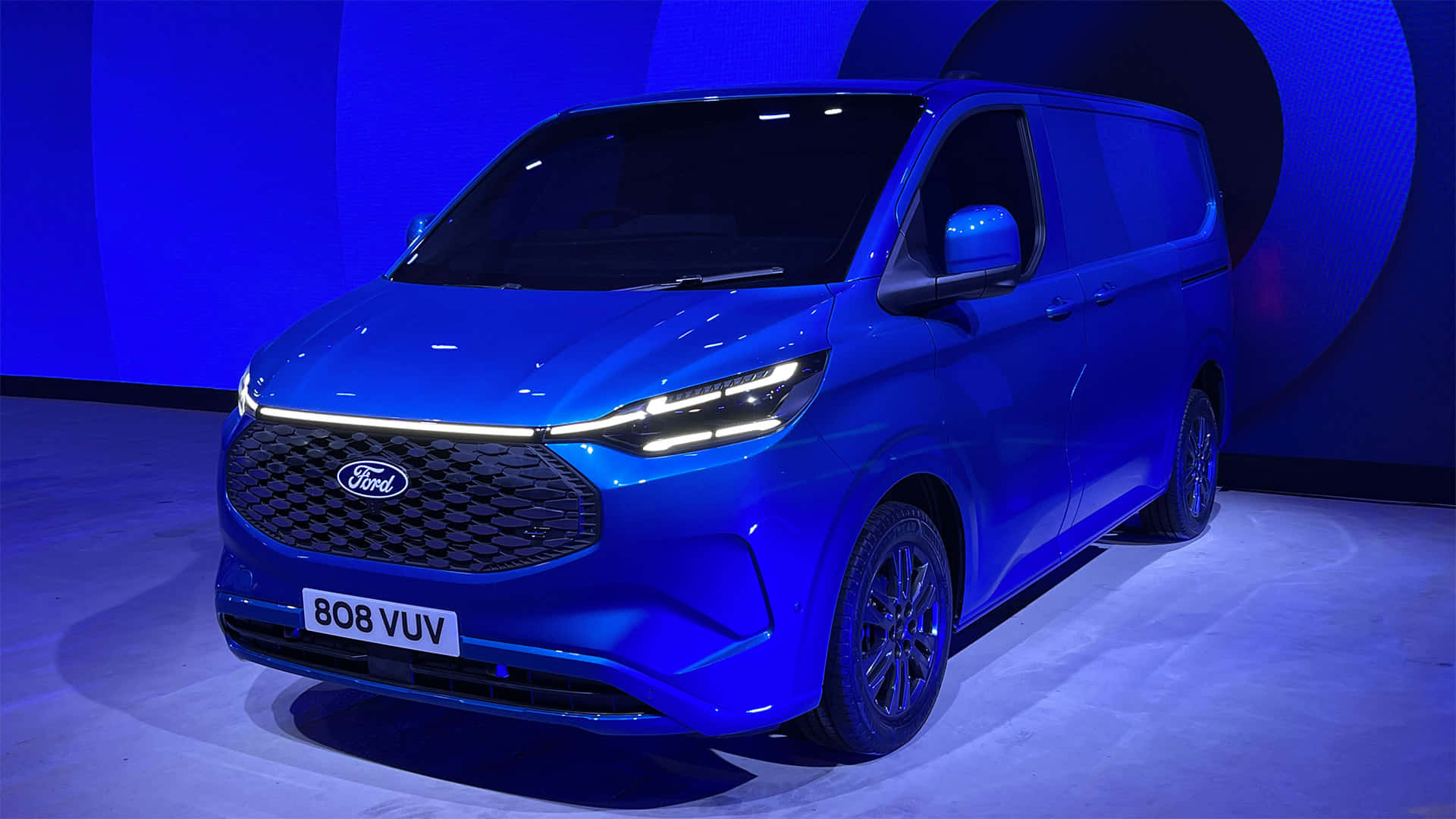Ford Transit 桌布 壁紙 — 一架時尚的藍色福特客貨車在產品發佈活動的戲劇性舞台燈光下閃閃發光。