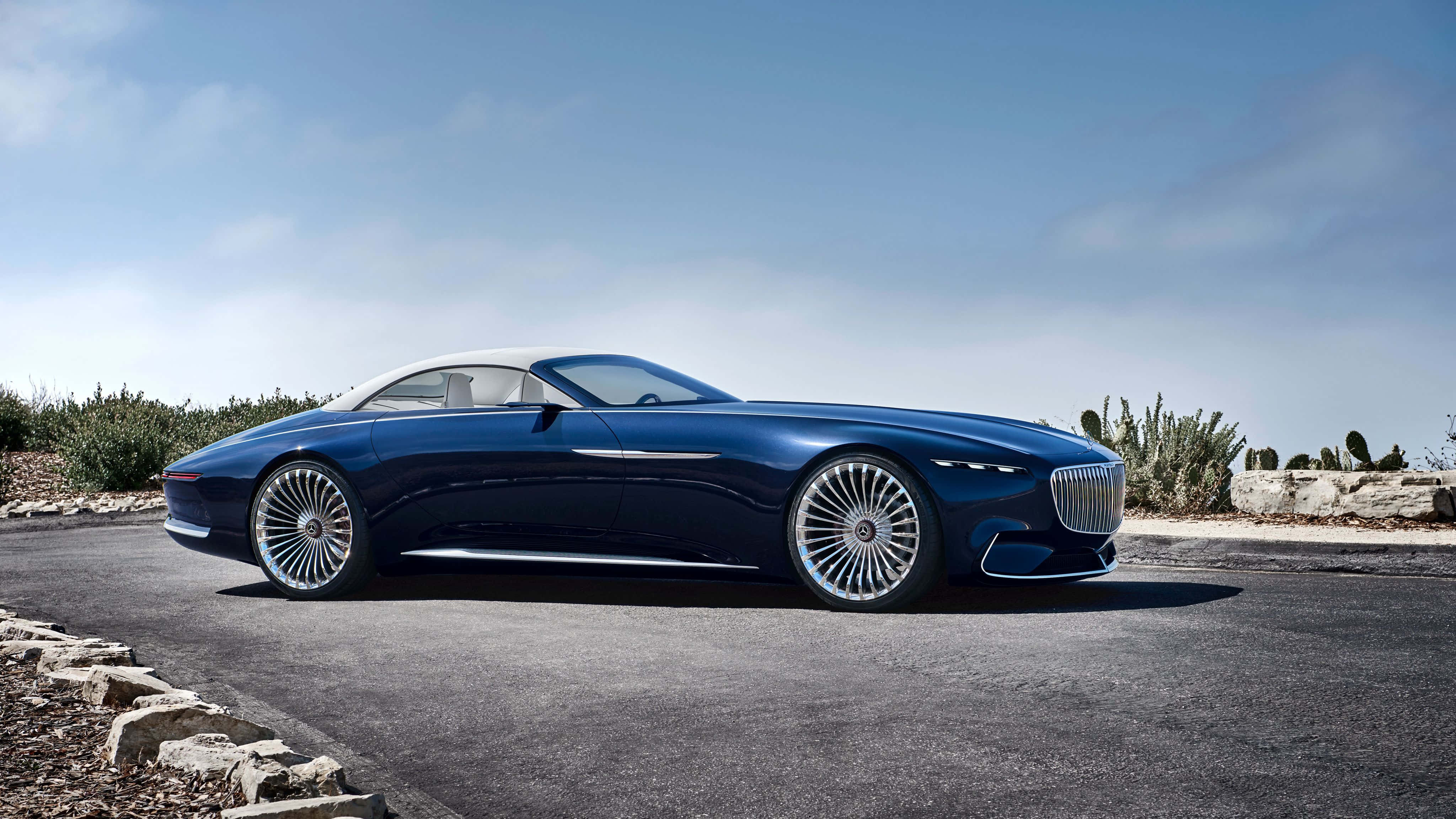 Maybach 桌布 壁紙 — 一架時尚的藍色豪華開篷跑車，白色車頂，停在鋪砌的道路上，旁邊是沙漠仙人掌，天空清澈湛藍。