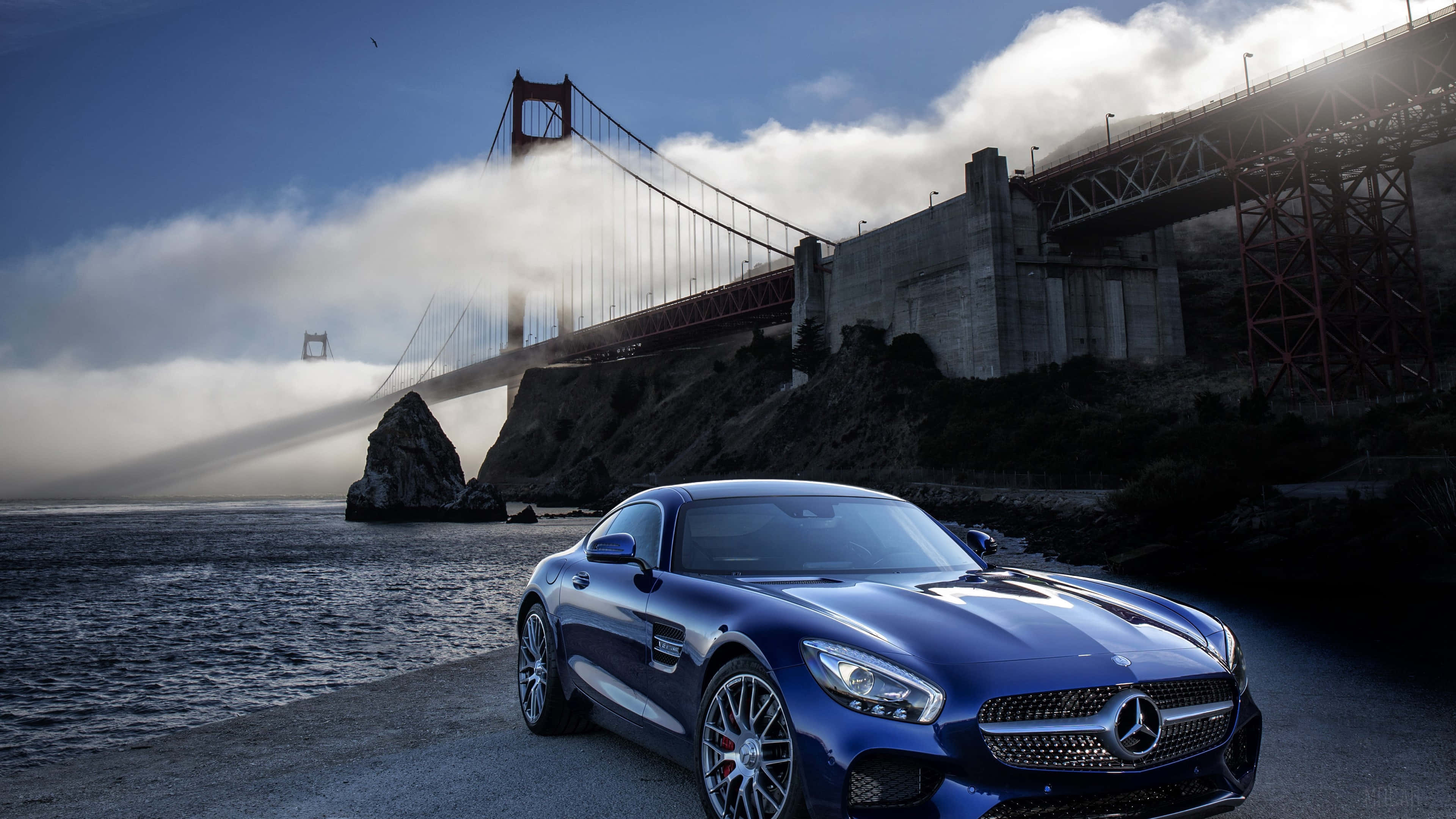 4K Mercedes 桌布 壁紙 — 一架時尚的藍色跑車停在水邊，背景是部分被霧籠罩的金門大橋。