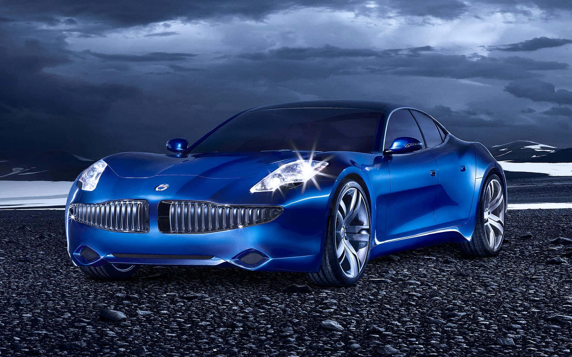 Fisker 桌布 壁紙 — 一架時尚的藍色跑車在戲劇性的暴風雲下，在碎石平原上閃閃發光，遠處有雪山。
