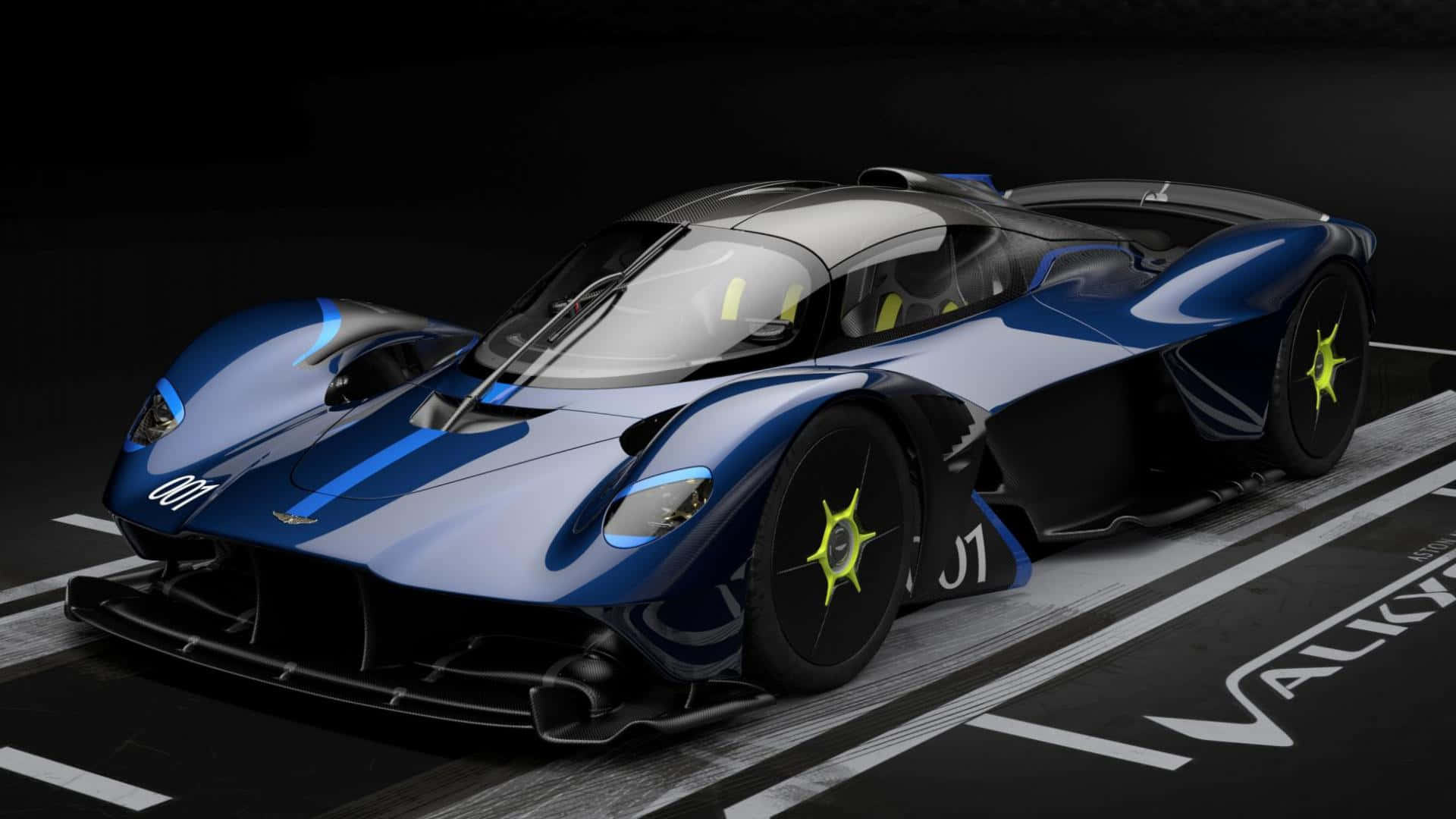 Aston Martin Valkyrie 桌布 壁紙 — 一架時尚的藍黑配色 Aston Martin Valkyrie 超跑，配備螢光黃色車輪，停泊在印有其名字的賽道上。