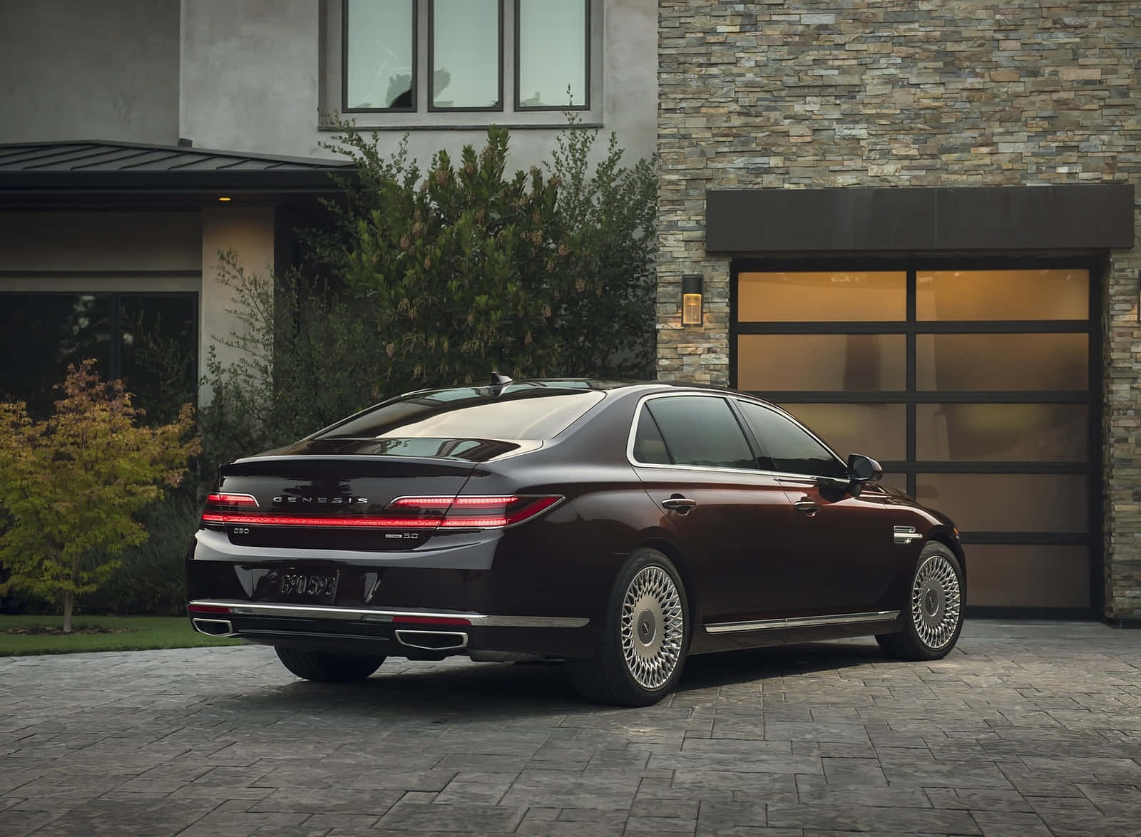 Genesis G90 桌布 壁紙 — 一架時尚的酒紅色Genesis G90豪華轎車停泊在現代石頭和玻璃屋前的石頭車道上。