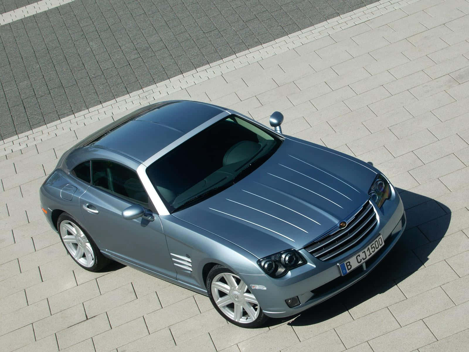Chrysler Crossfire 桌布 壁紙 — 一架時尚的銀色 Chrysler Crossfire 跑車停泊在淺灰色磚砌路面上，在明亮的日光下。