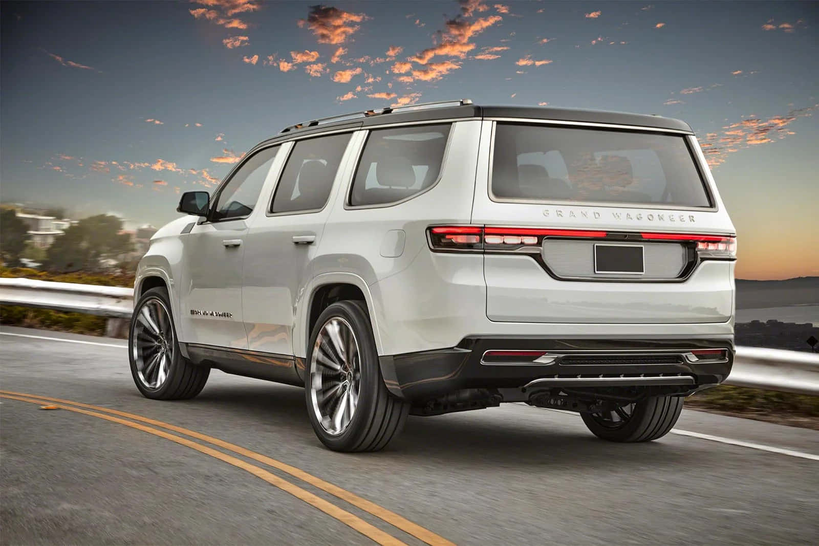 Jeep Wagoneer 桌布 壁紙 — 一架時尚的銀色 Grand Wagoneer SUV 沿著海岸公路在日落時分巡航，頭頂是鮮豔的橙色雲彩。