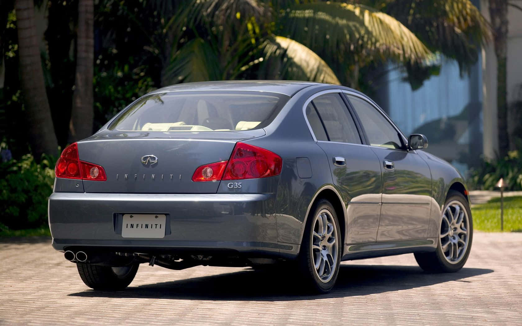 Infiniti G35 桌布 壁紙 — 一架時尚的銀色 Infiniti G35 房車停泊在陽光普照的磚砌車道上，背景有棕櫚樹和茂密的綠植。