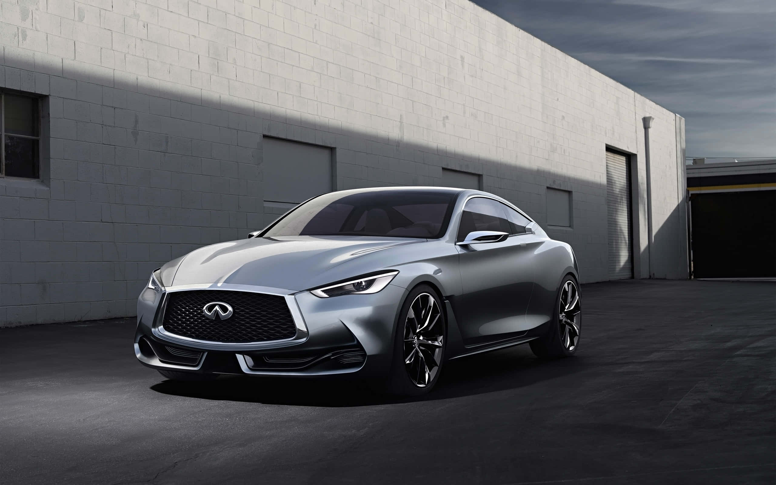 Infiniti Q60 桌布 壁紙 — 一架時尚的銀色 Infiniti 跑車停泊在純白色磚砌倉庫前，燈光效果極具戲劇性。