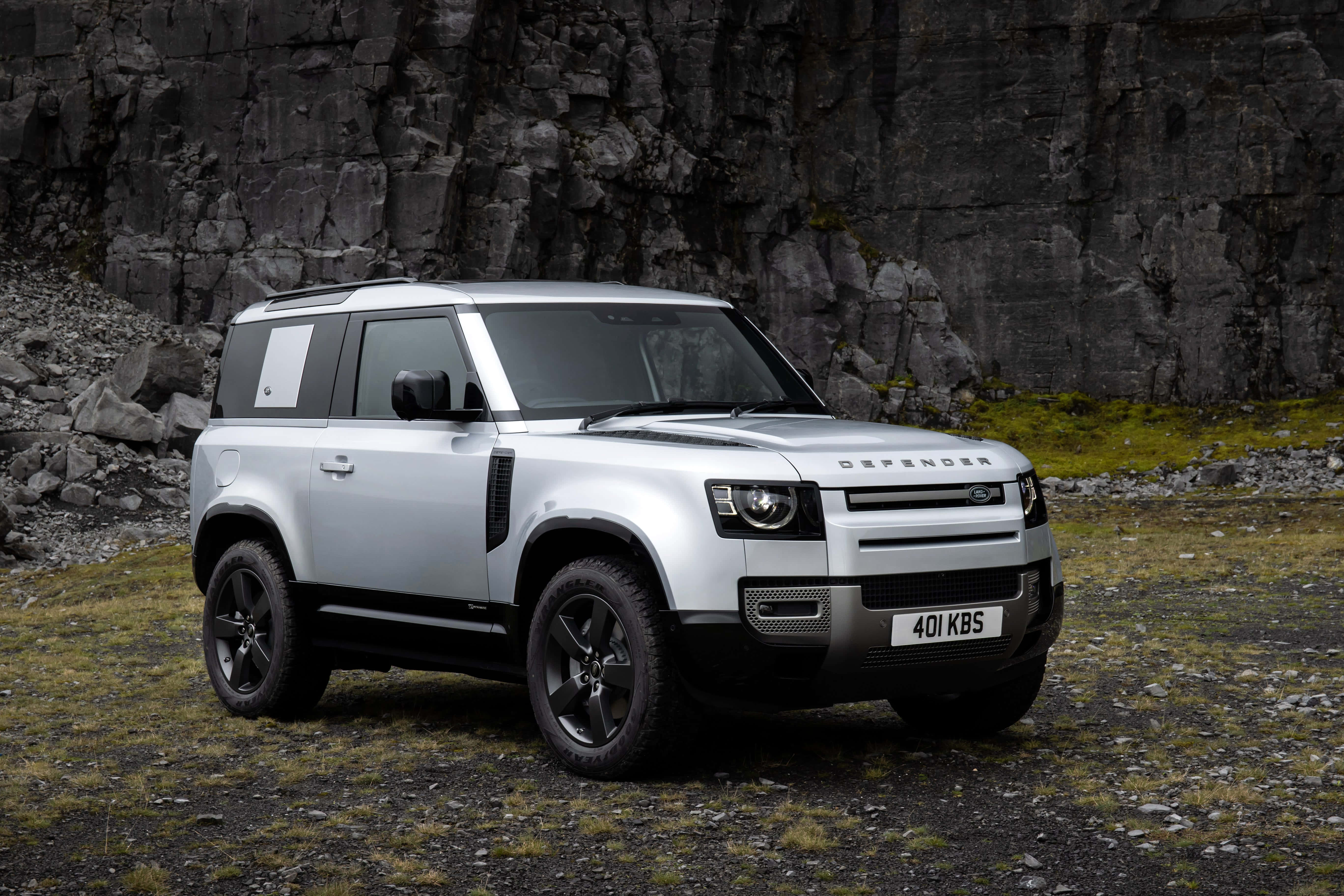 Land Rover Defender 桌布 壁紙 — 一架時尚的銀色 Land Rover Defender 在崎嶇地形上，聳立於高聳的黑色岩壁前。