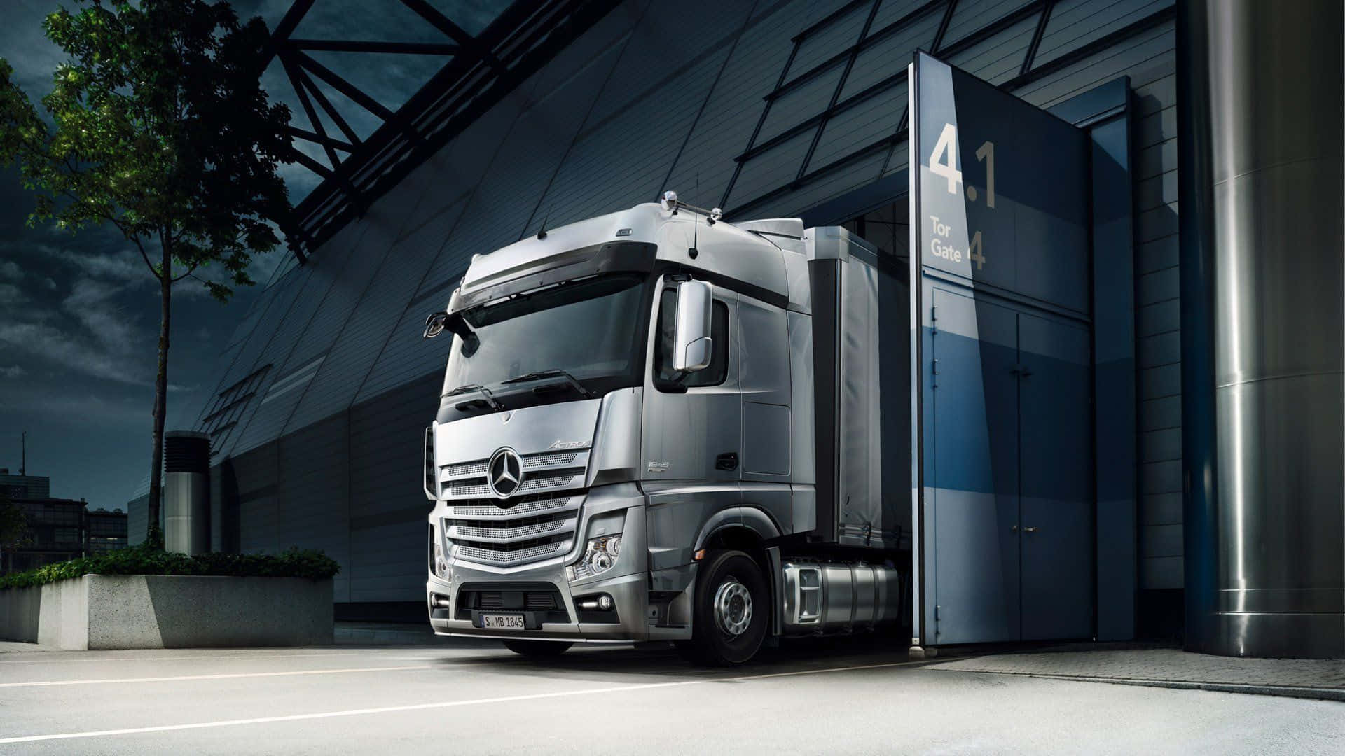 貨車 桌布 壁紙 — 一架時尚的銀色 Mercedes-Benz 半掛卡車停泊在現代工業裝卸區，背景是陰鬱的暮色天空。