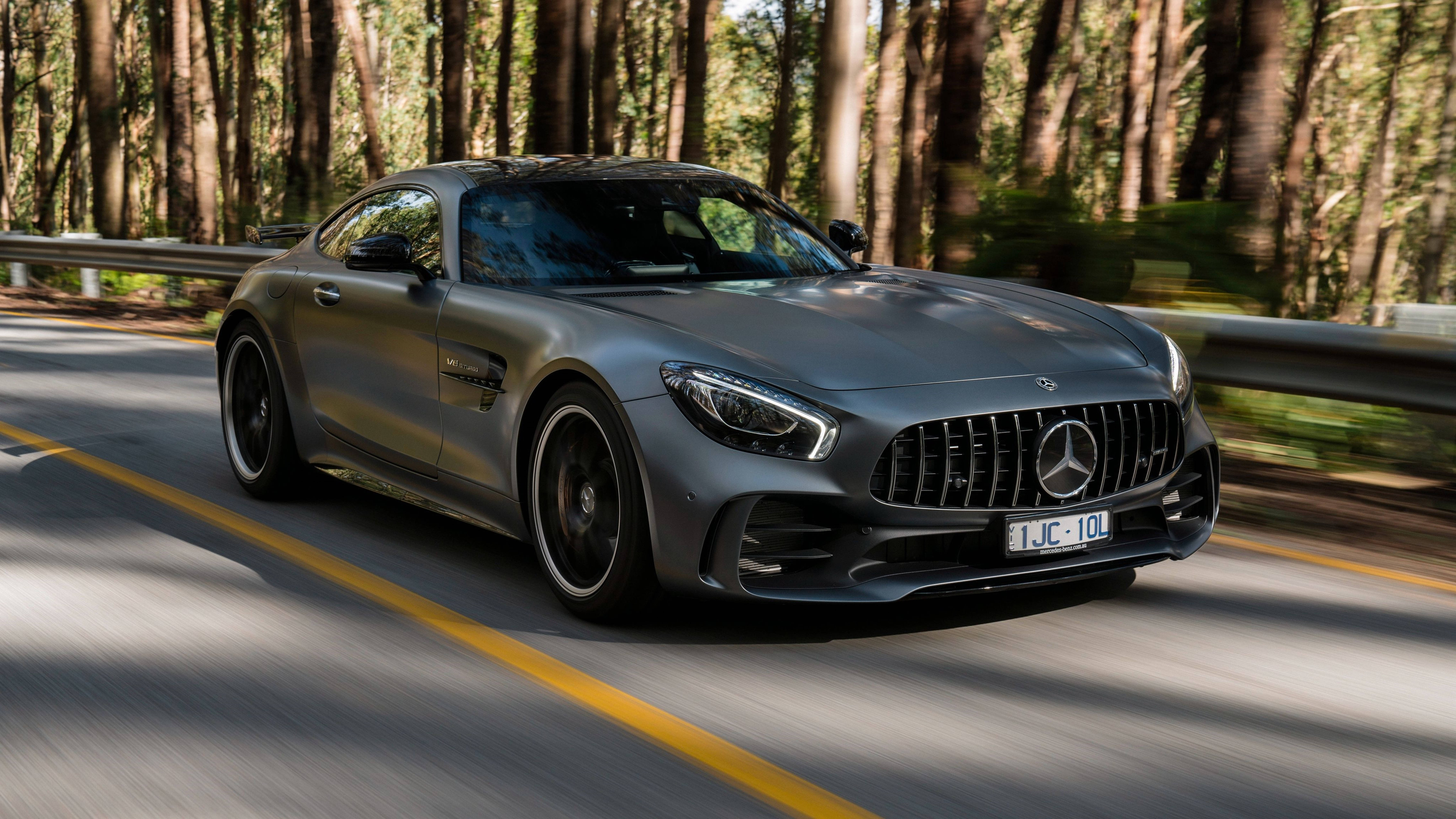 Mercedes 桌布 壁紙 — 一架時尚的銀色 Mercedes-AMG GT R 在陽光明媚的森林道路上疾馳，樹木和瀝青路面呈現動態模糊效果。