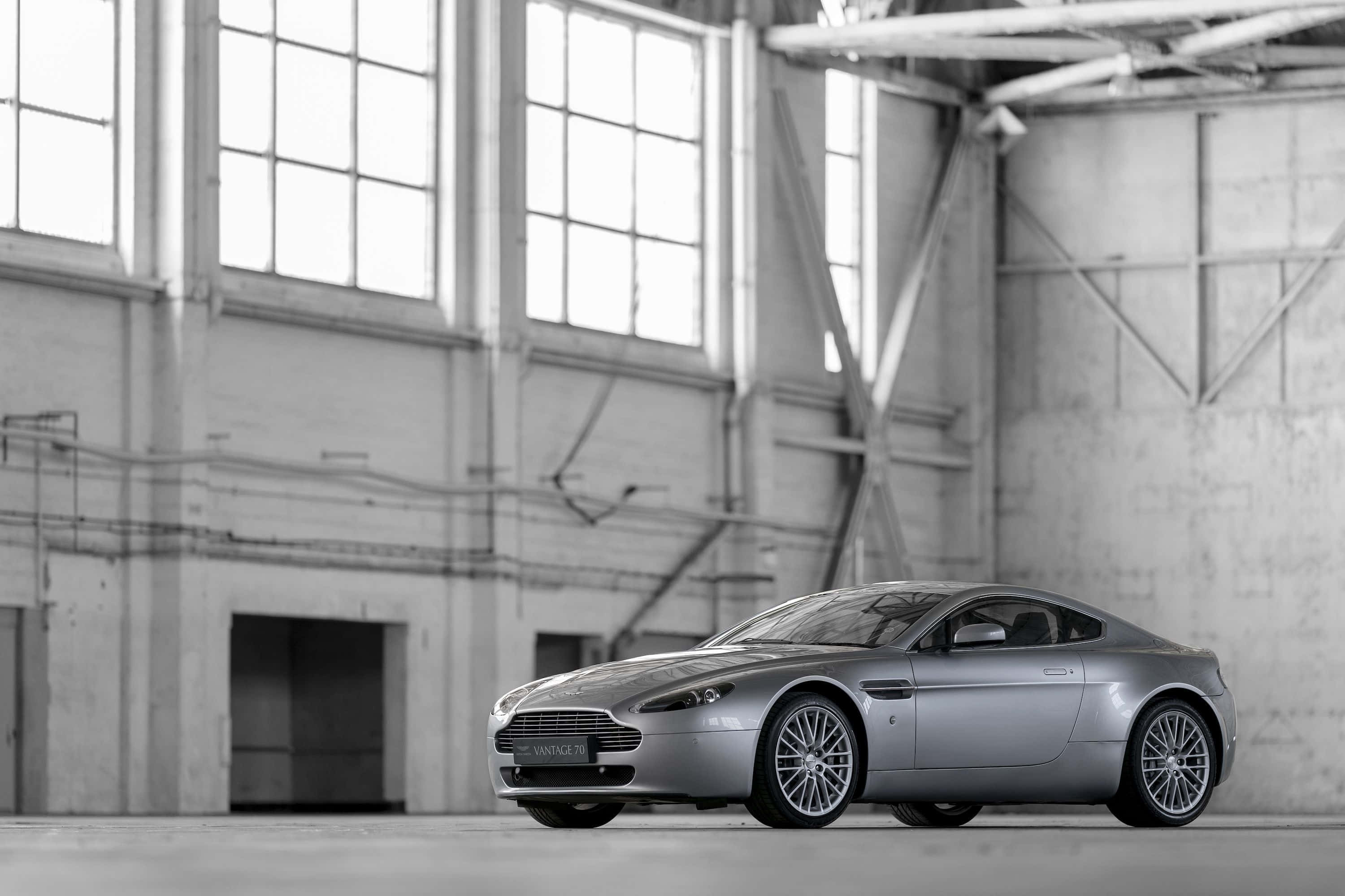 Aston Martin V12 Vantage 桌布 壁紙 — 一架時尚的銀色Aston Martin Vanquish跑車停泊在寬敞的高窗工業倉庫內。