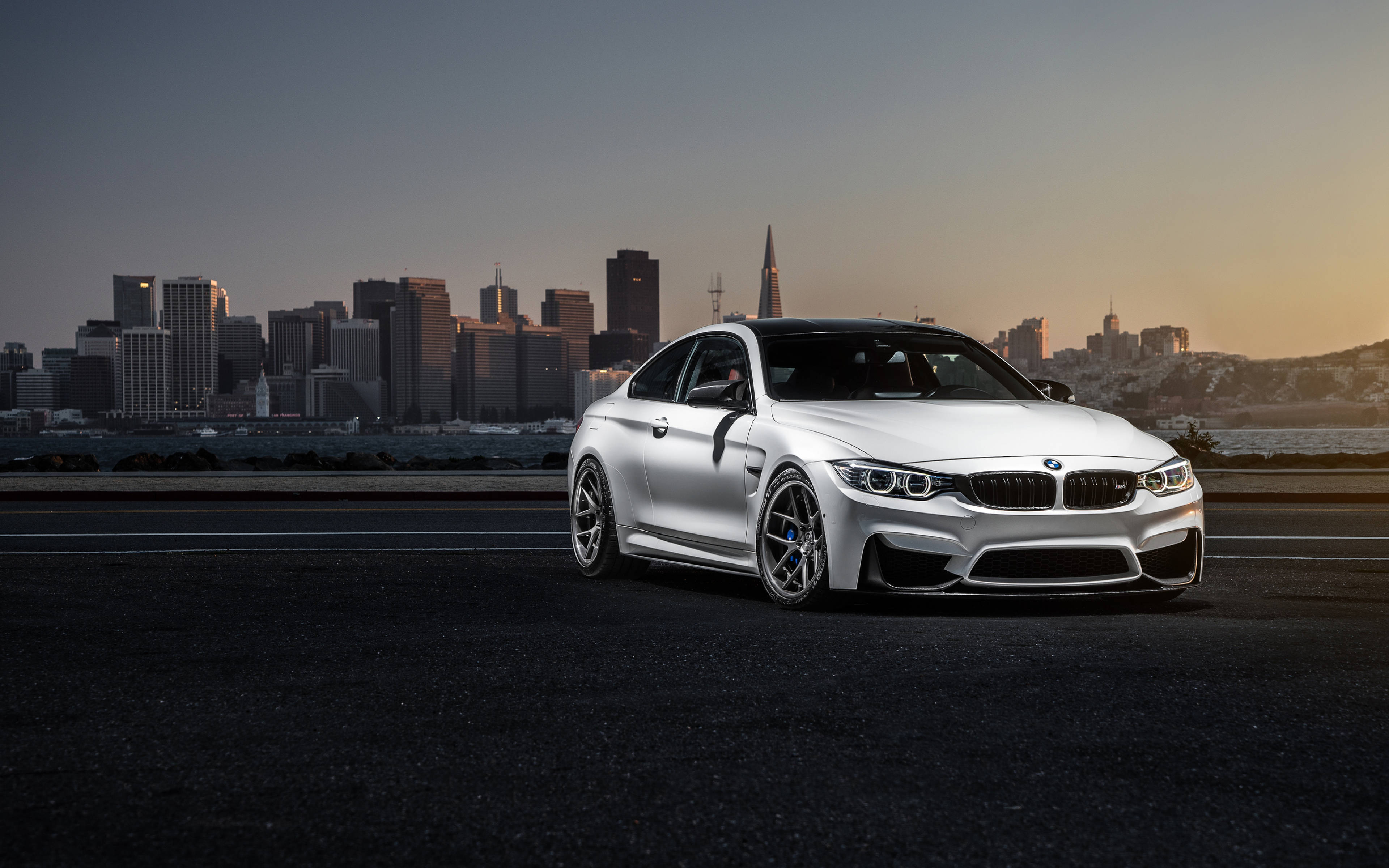 Bmw M Series 桌布 壁紙 — 一架時尚的銀色BMW M4雙門轎跑車停在高速公路上，三藩市天際線在日落時分閃耀著光芒。