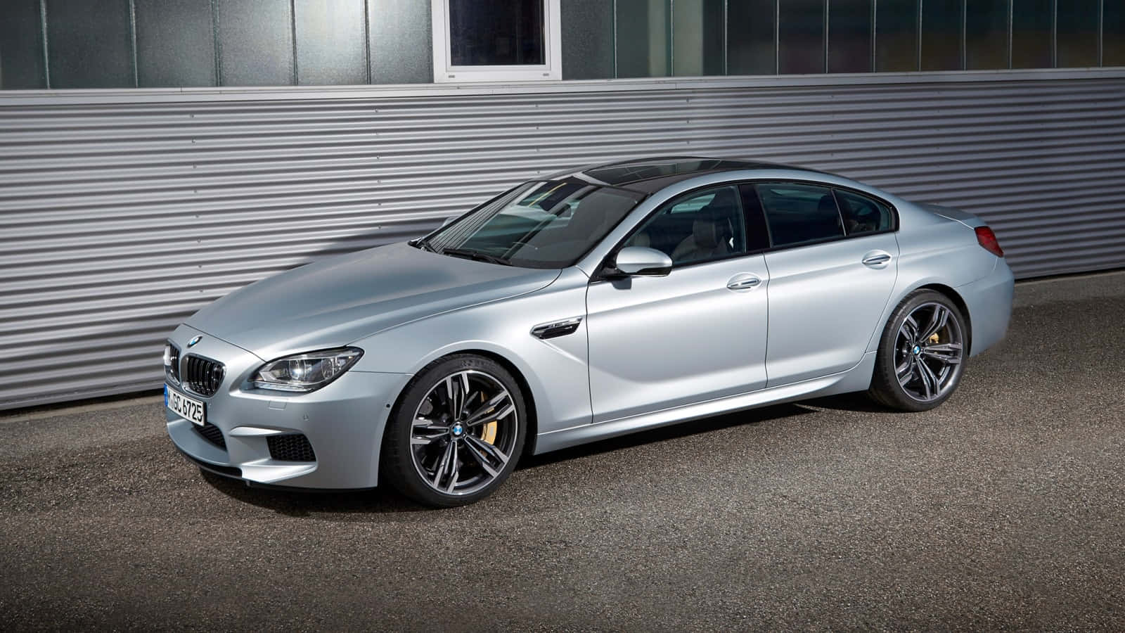 Bmw M6 桌布 壁紙 — 一架時尚的銀色BMW M6跑車在明亮的日光下停泊在波紋金屬牆旁。