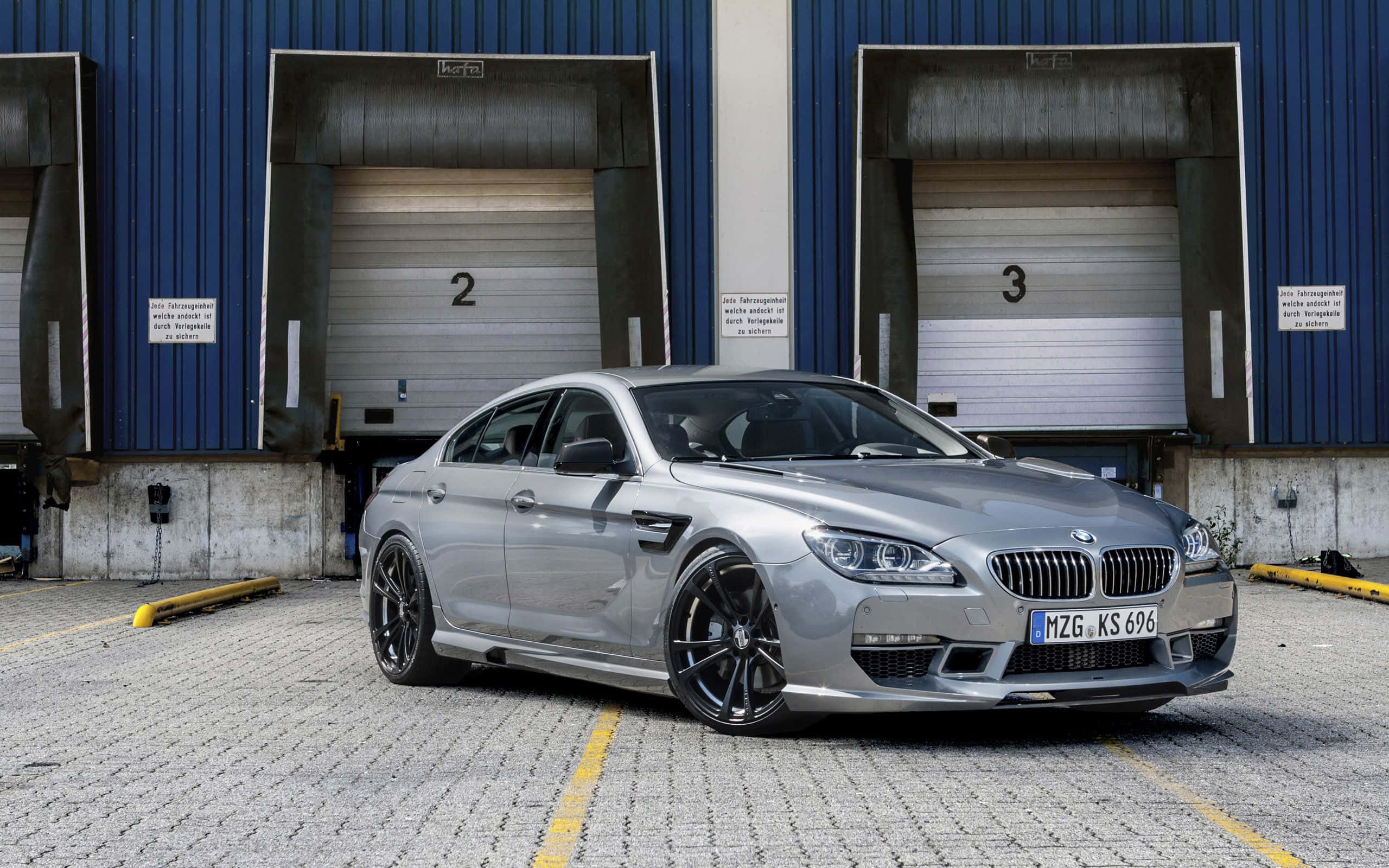 Bmw 6 Series 桌布 壁紙 — 一架時尚的銀色BMW M6轎跑車停在工業藍色倉庫門前的鋪砌場地上。
