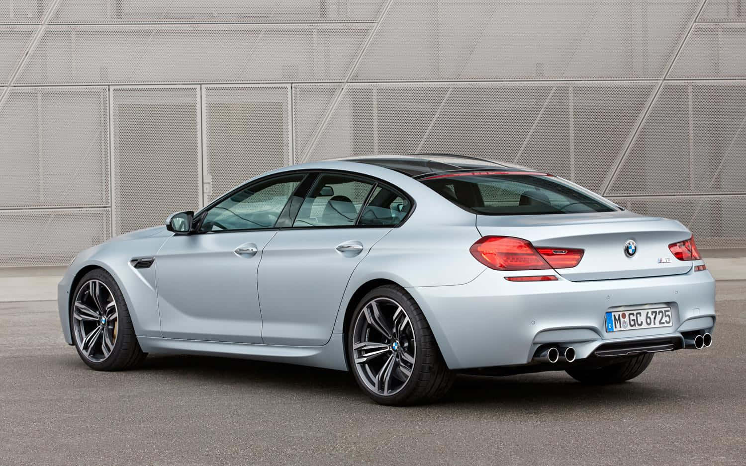 Bmw M6 桌布 壁紙 — 一架時尚的銀色BMW M6轎跑車停泊在現代金屬網牆前，展示其運動型設計和雙排氣管。