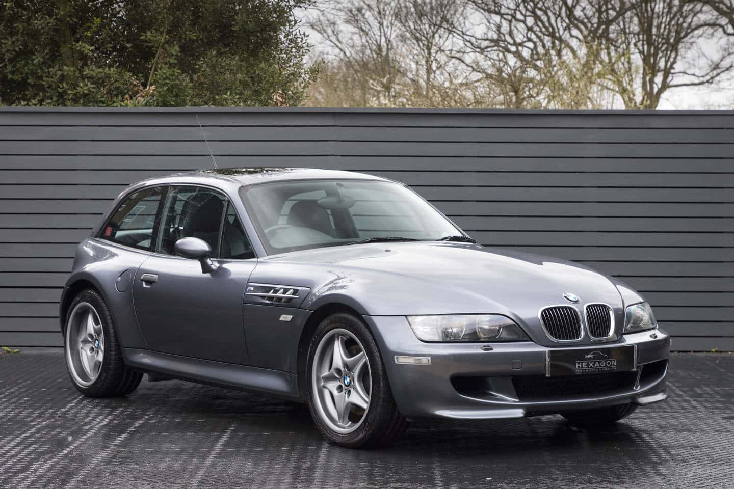 Bmw Z3 桌布 壁紙 — 一架時尚的銀色BMW Z3開篷跑車停泊在濕漉漉的路面上，背景是深灰色條紋牆壁和光禿禿的樹木。