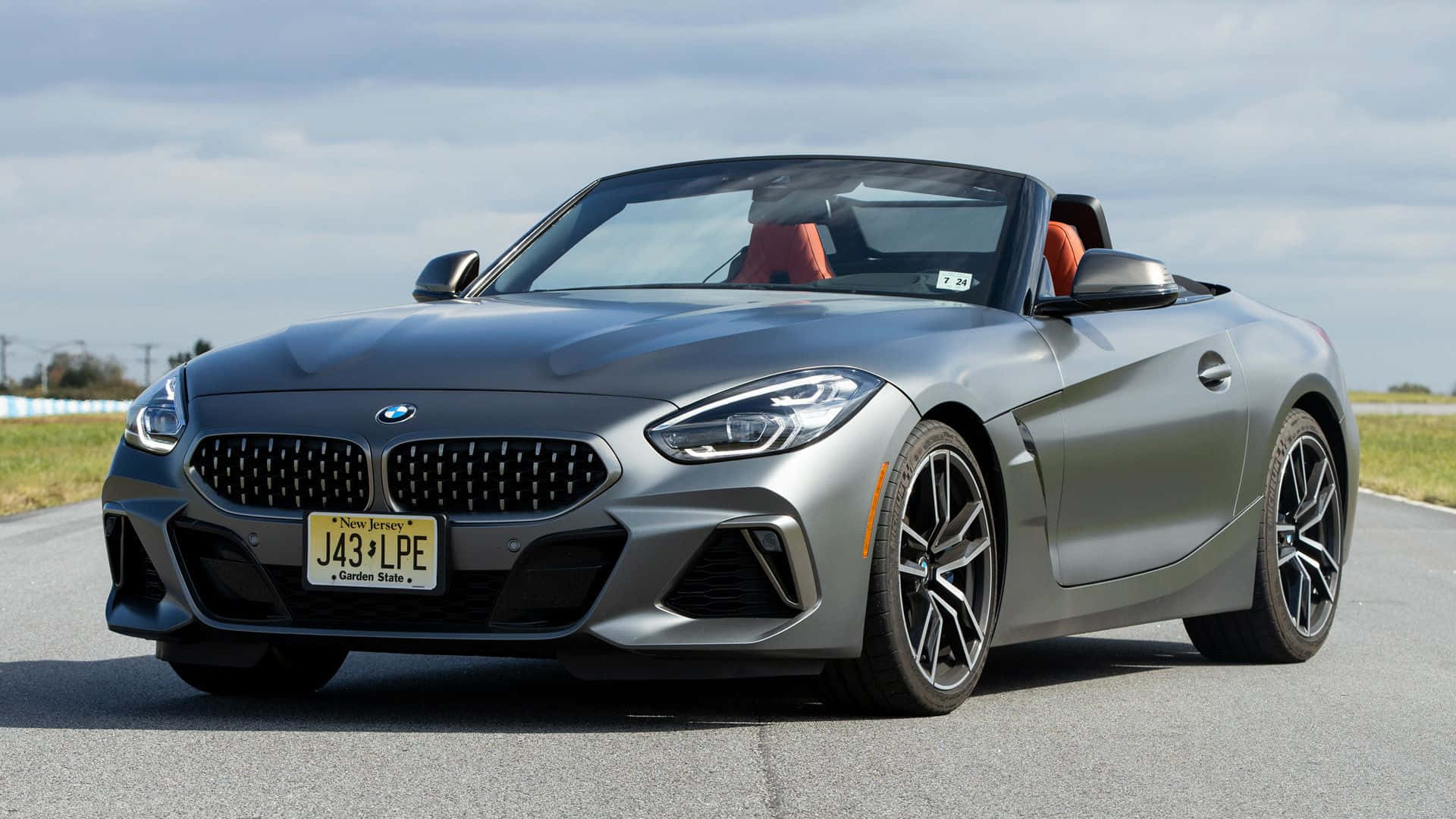 Bmw Z4 桌布 壁紙 — 一架時尚的銀色BMW Z4開篷跑車停泊在開闊的道路上，天空多雲，可見橙色內飾座椅。