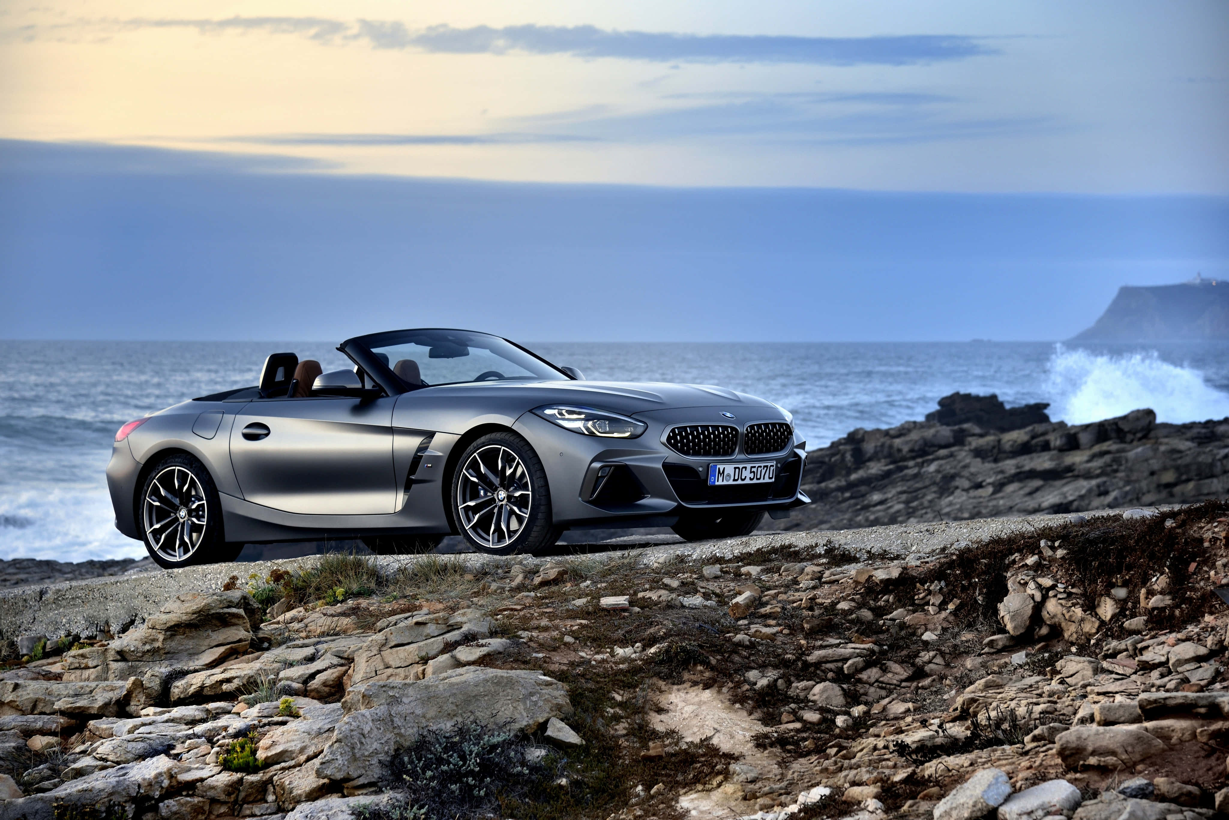 Bmw Z4 桌布 壁紙 — 一架時尚的銀色BMW Z4開篷跑車停泊在崎嶇的海岸懸崖上，俯瞰著黃昏時分洶湧的海浪。