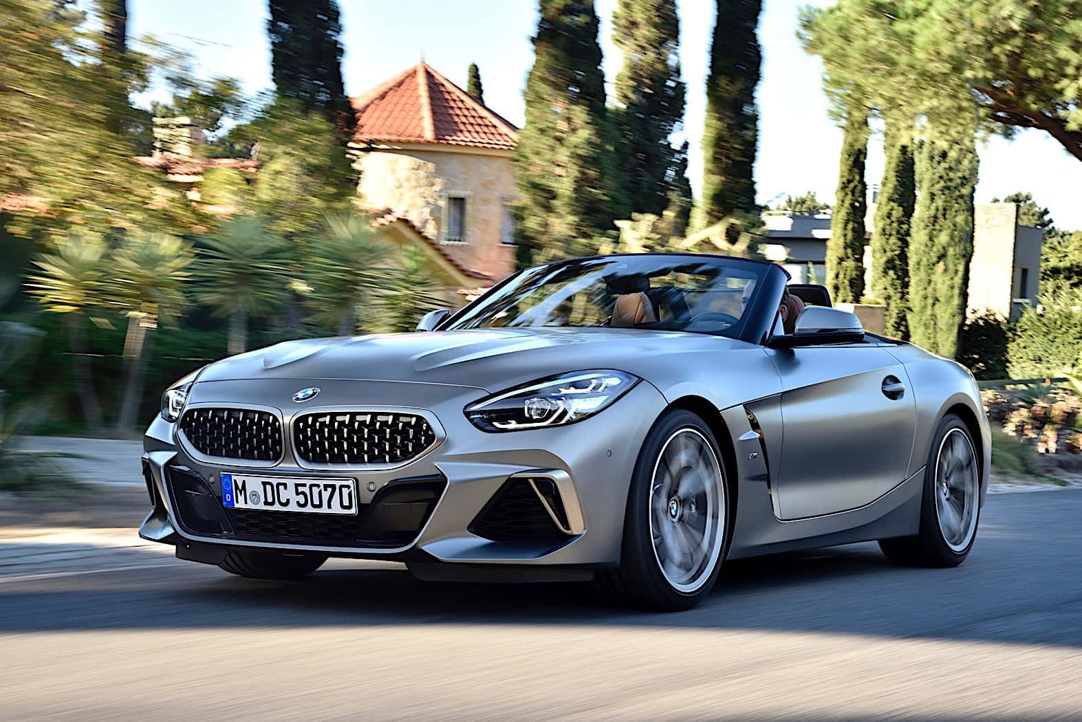 Bmw Z4 桌布 壁紙 — 一架時尚的銀色BMW Z4開篷跑車在陽光明媚的道路上飛馳，兩旁種滿高大的柏樹和地中海風格的房屋。