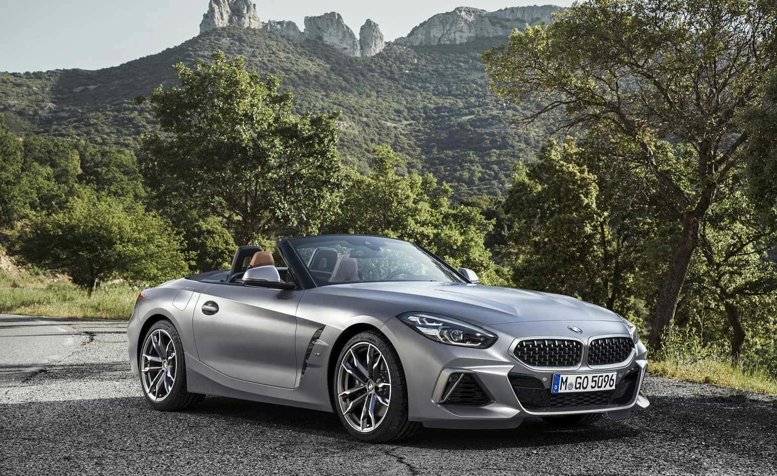 Bmw Z4 桌布 壁紙 — 一架時尚的銀色BMW Z4開篷車停在碎石路上，背景是茂密的綠樹和岩石山脈。