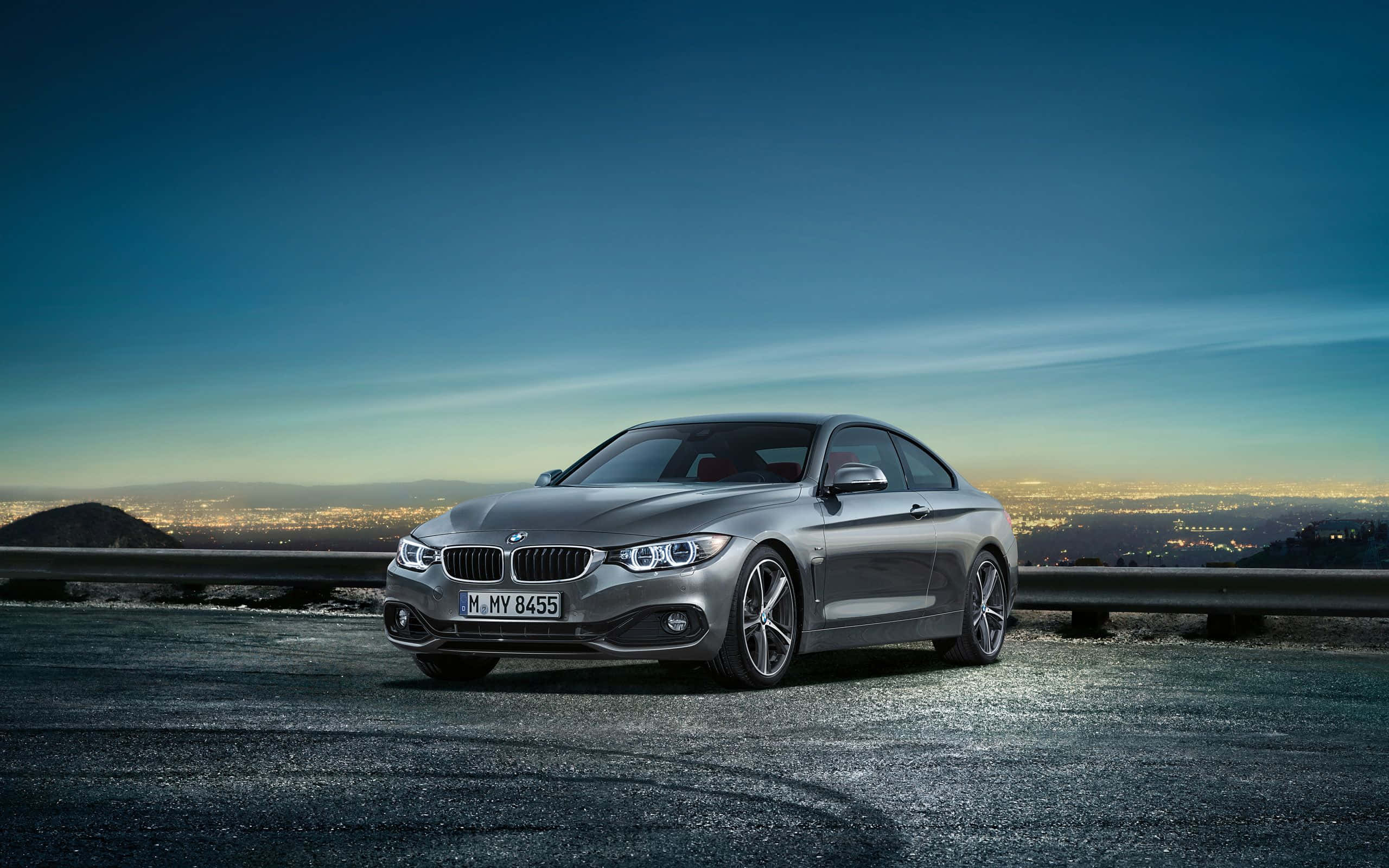 Bmw 4 Series 桌布 壁紙 — 一架時尚的銀色BMW雙門跑車停泊在黃昏的山路上，下方是閃爍的城市景觀。