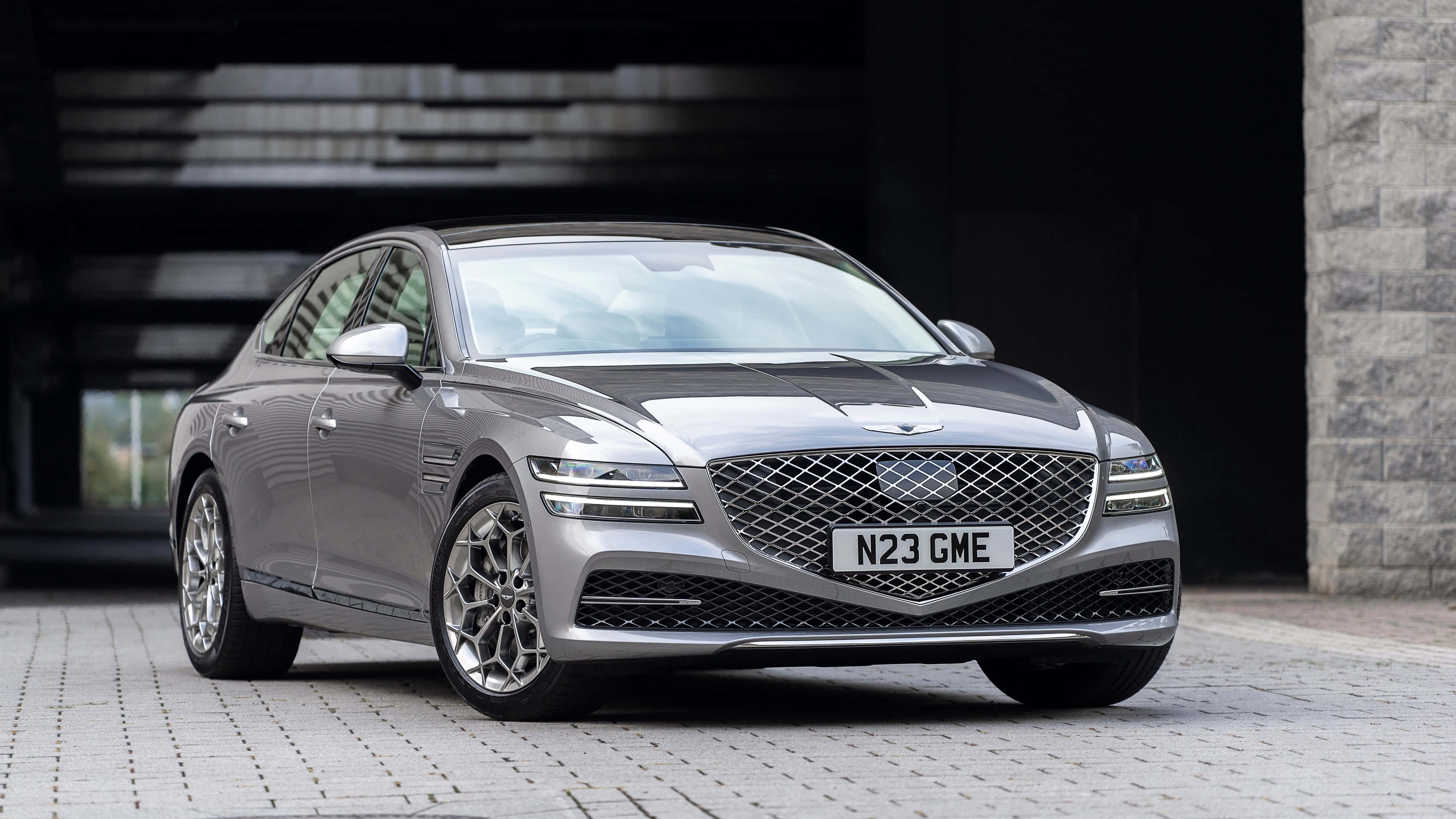 Genesis G80 桌布 壁紙 — 一架時尚的銀色Genesis G90豪華轎車停泊在現代建築結構下的石頭車道上。