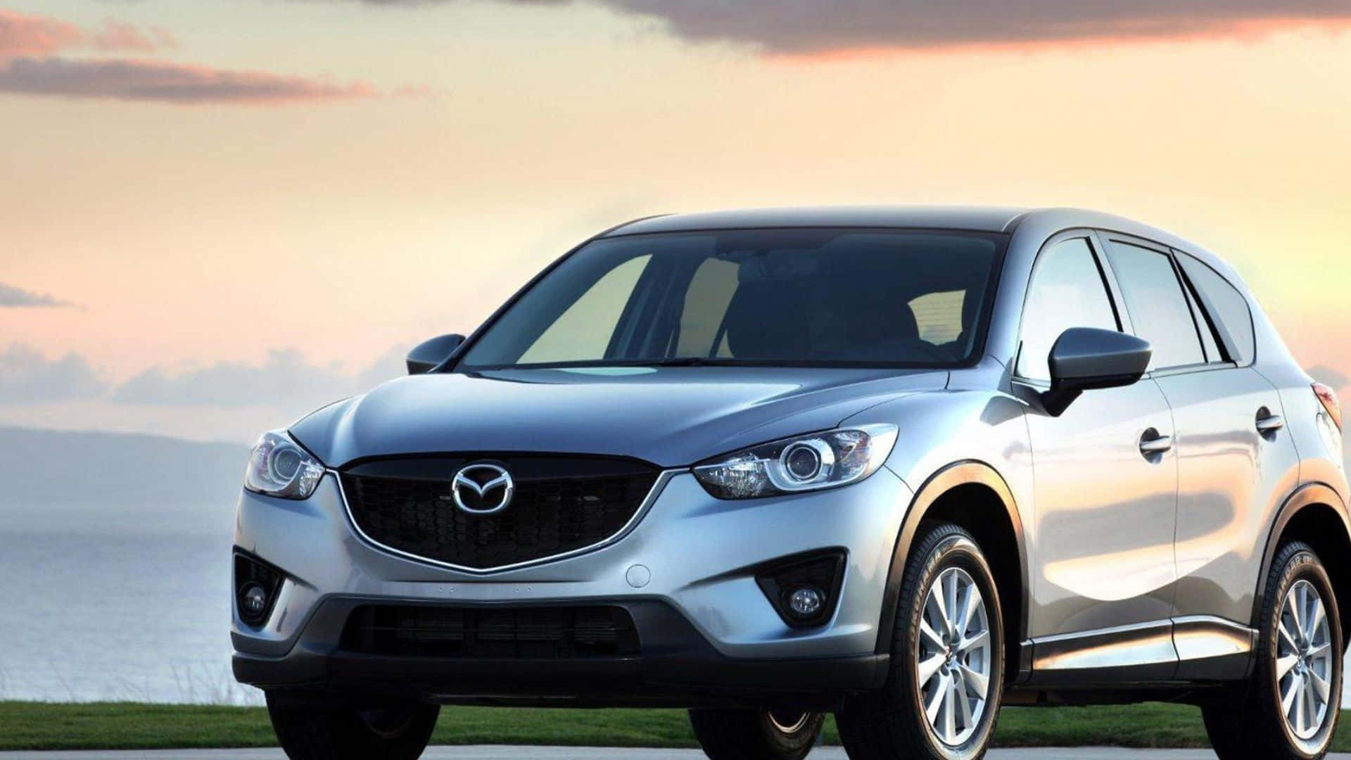 Mazda Cx-5 桌布 壁紙 — 一架時尚的銀色Mazda CX-5 SUV停泊在日落時分的海邊，溫暖的金色光線在其拋光表面上反射。