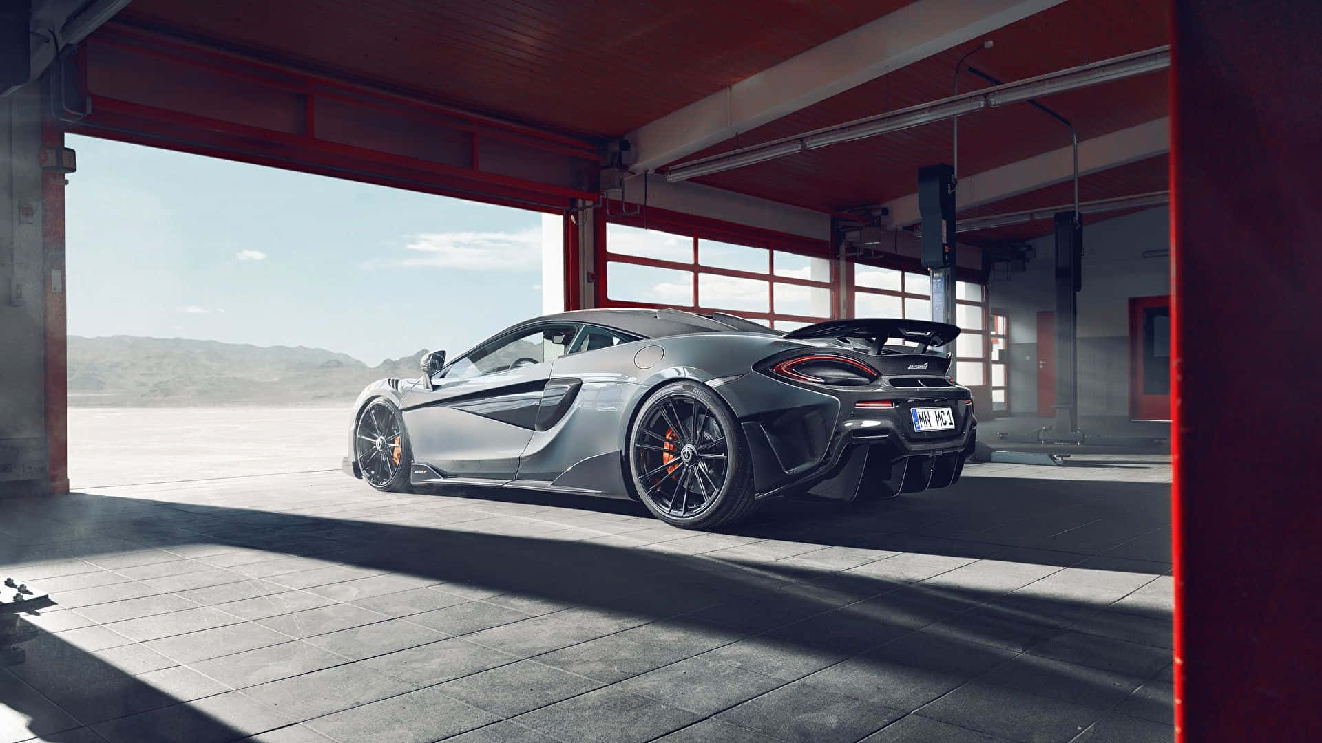 Garage 桌布 壁紙 — 一架時尚的銀色McLaren跑車停泊在紅色工業車庫中，陽光從敞開的門照射進來。