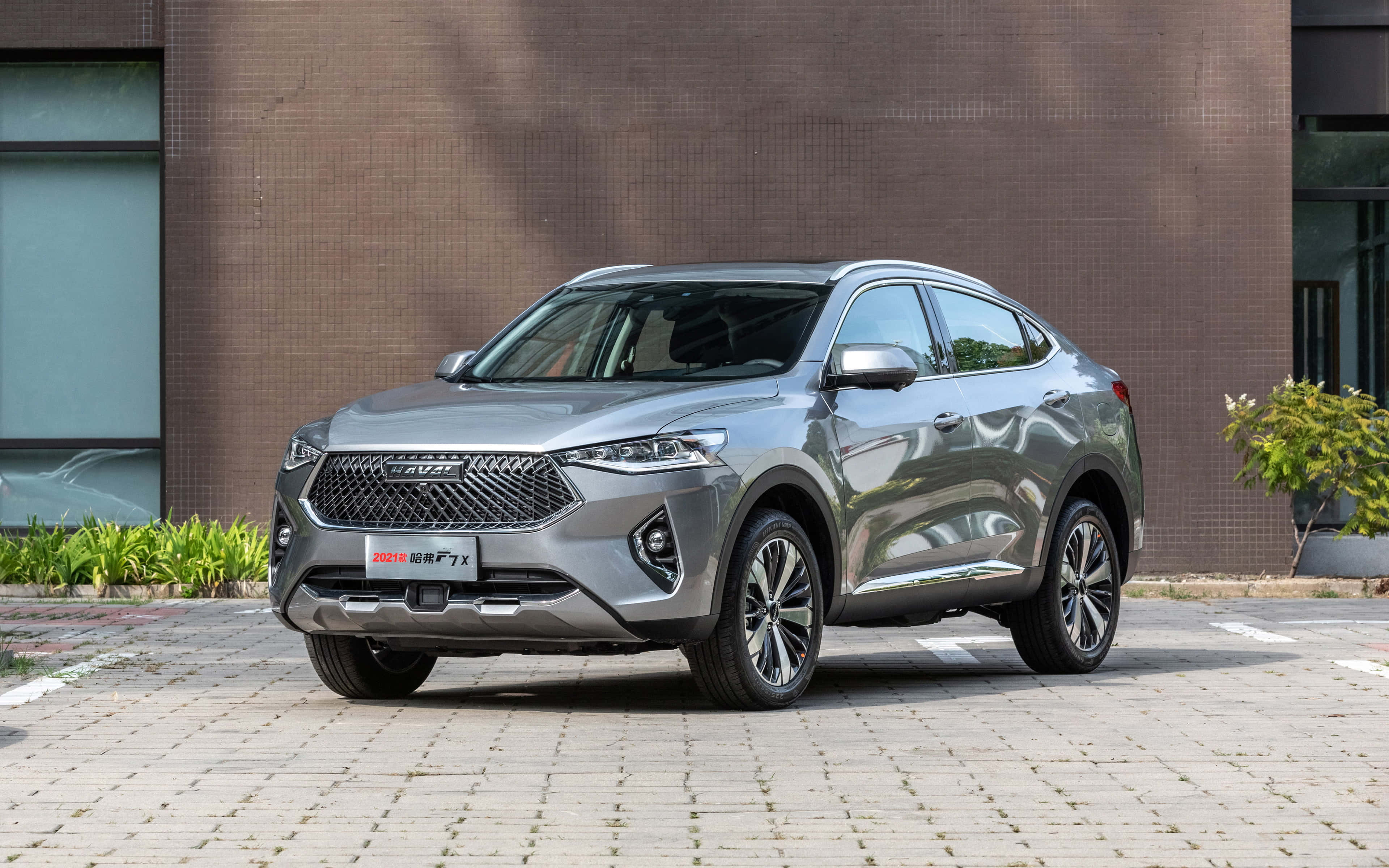 Haval 桌布 壁紙 — 一架時尚的銀色SUV停泊在鋪砌的庭院中，背景是現代磚砌建築和綠植。