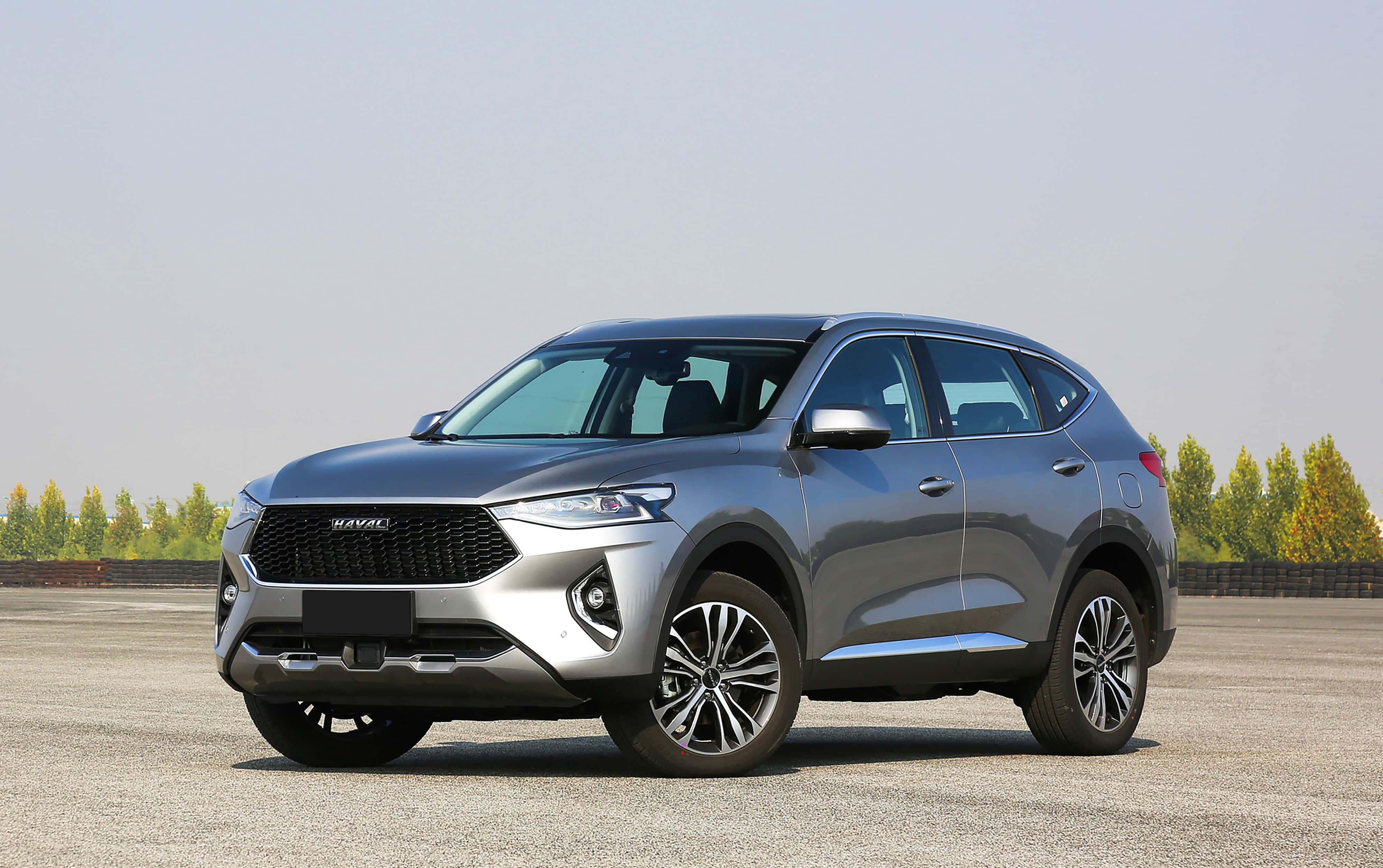 Haval 桌布 壁紙 — 一架時尚的銀色哈弗SUV停泊在開闊的瀝青停車場上，背景有樹木，天空晴朗。