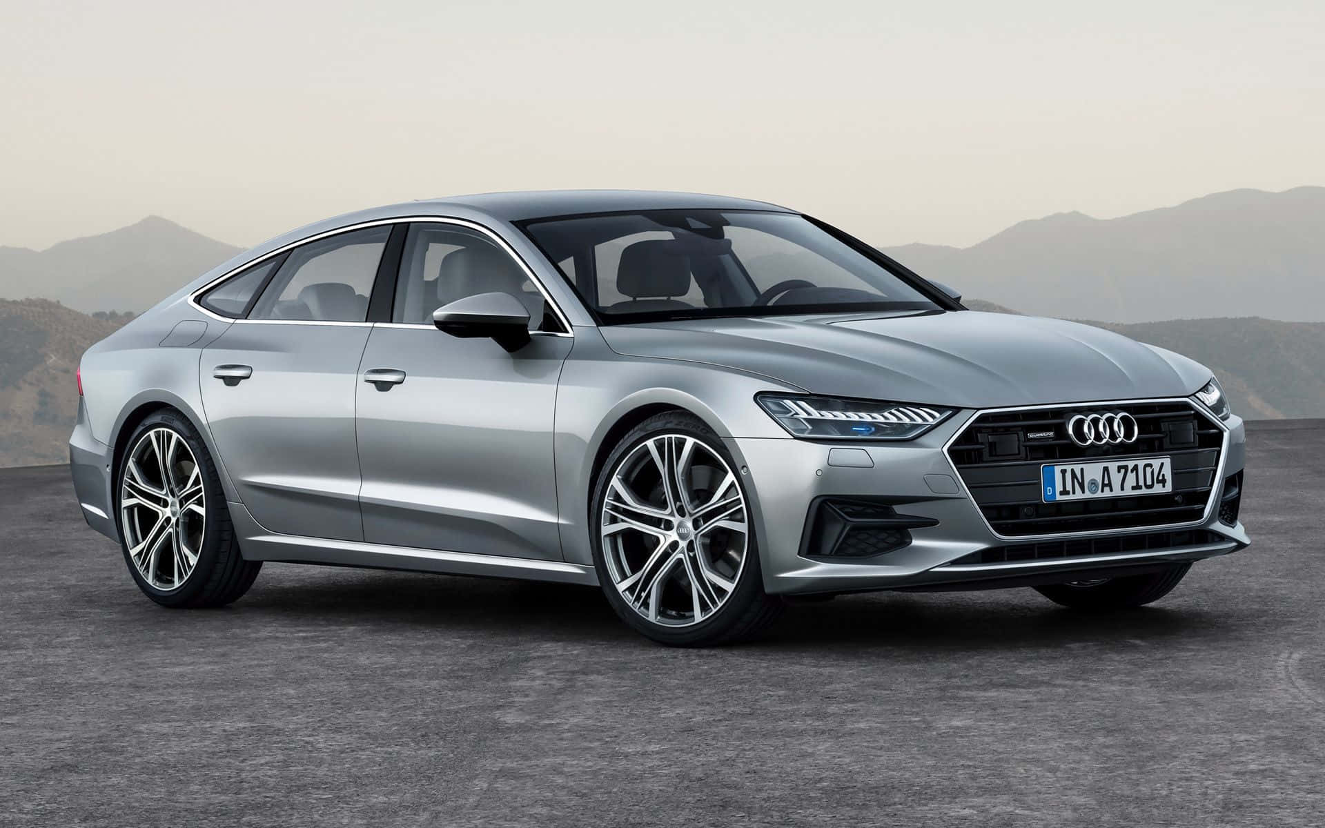 Audi S7 桌布 壁紙 — 一架時尚的銀色奧迪A7 Sportback停泊在鋪砌路面上，背景是朦朧的山巒，柔和日光下。