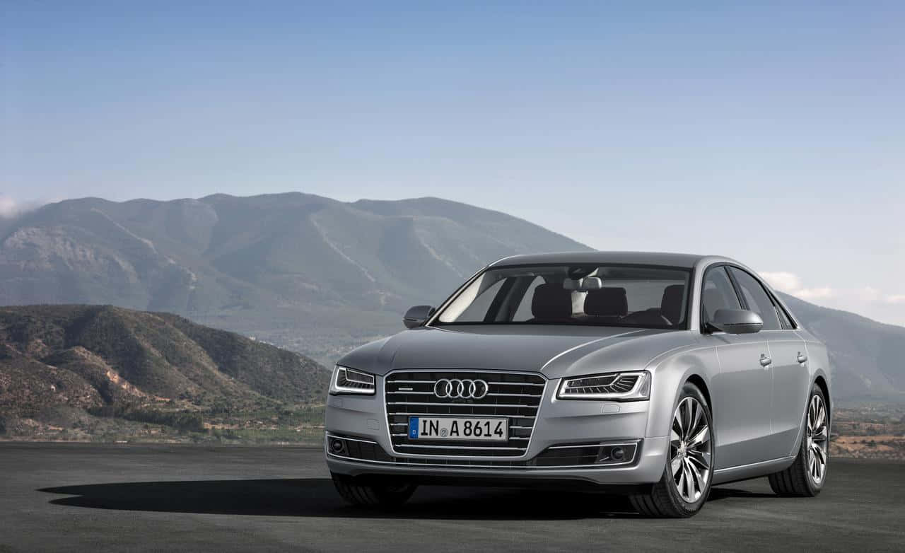 Audi S8 桌布 壁紙 — 一架時尚的銀色奧迪A8房車停泊在鋪砌的觀景點上，遠山在晴朗的藍天下。