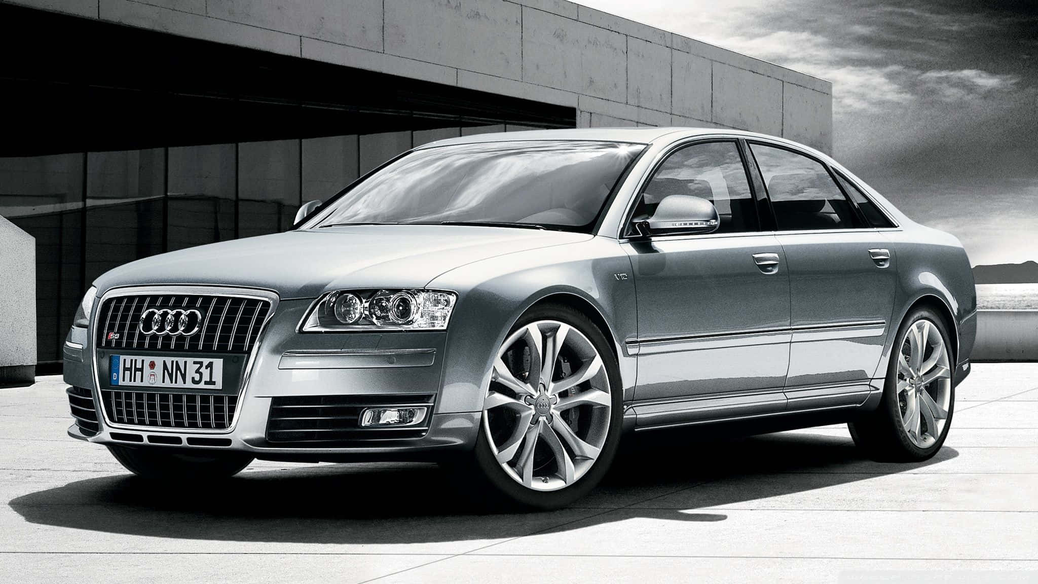 Audi S8 桌布 壁紙 — 一架時尚的銀色奧迪房車停泊在現代混凝土建築前，背景是戲劇性的多雲天空。