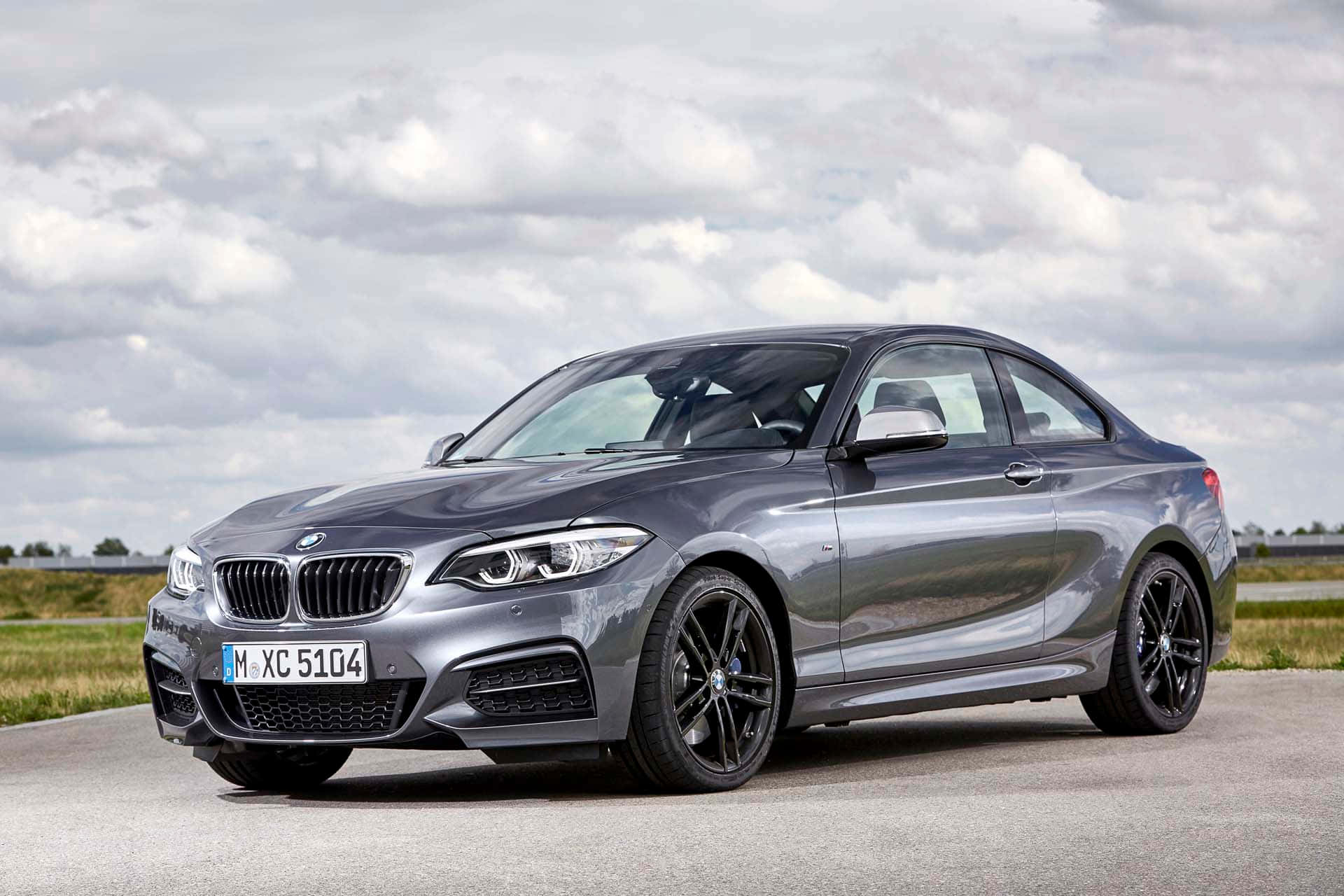Bmw 2 Series 桌布 壁紙 — 一架時尚的銀色寶馬2系轎跑車停在瀝青路上，天空多雲，背景是草地田野。
