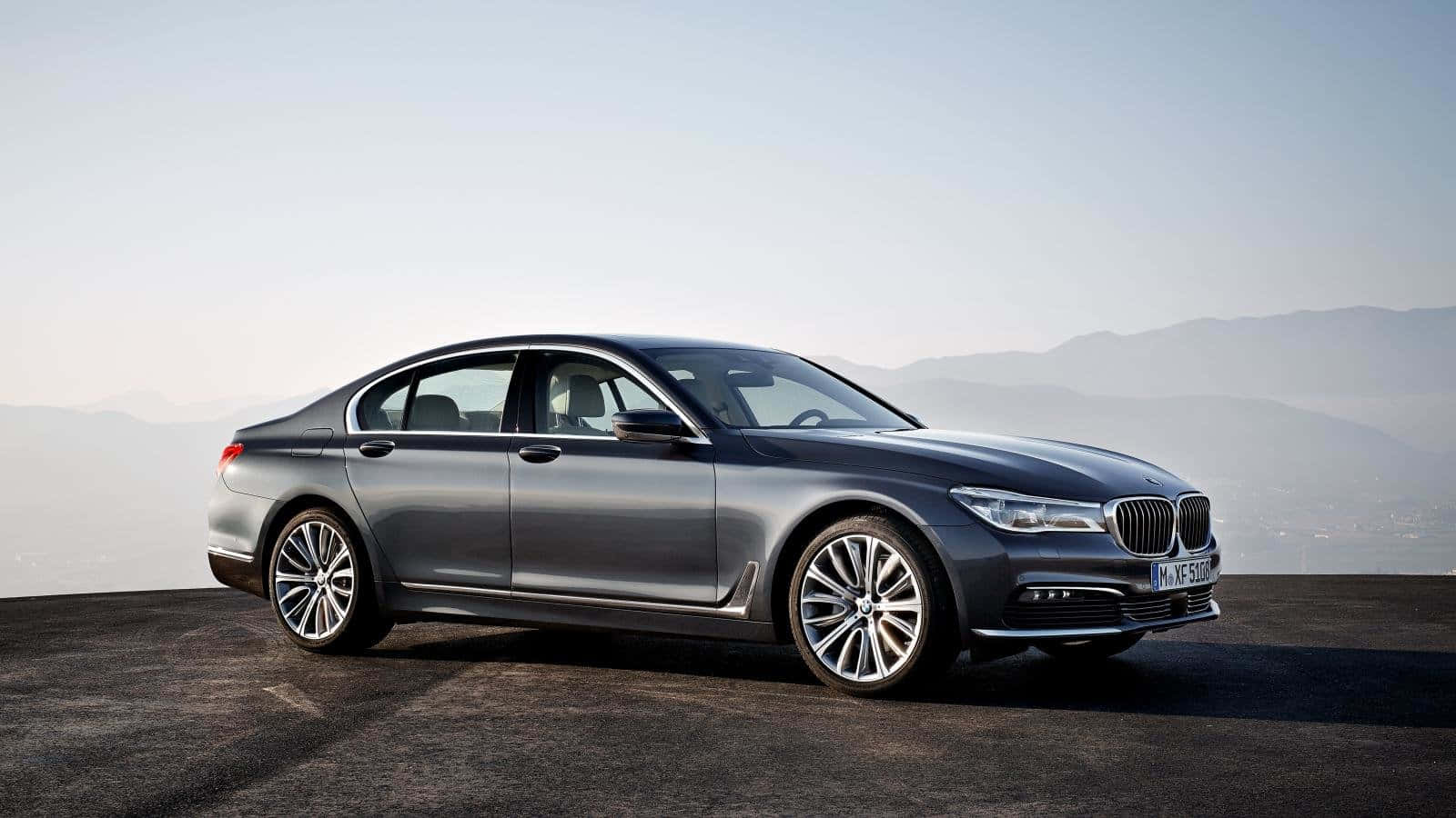 Bmw 7 Series 桌布 壁紙 — 一架時尚的銀色寶馬7系轎車停泊在懸崖上，俯瞰著朦朧天空下的遠山。