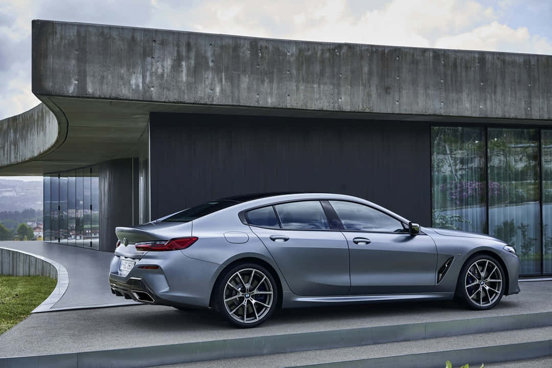Bmw 8 Series 桌布 壁紙 — 一架時尚的銀色寶馬8系轎跑車停泊在現代混凝土建築旁，建築有玻璃牆，天空多雲。