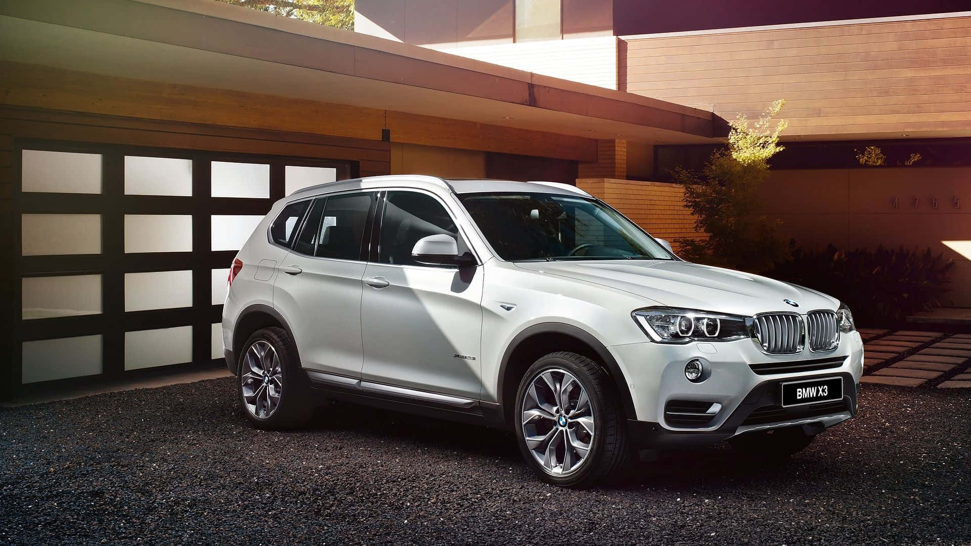 Bmw X3 桌布 壁紙 — 一架時尚的銀色寶馬X3 SUV停泊在碎石路上，前面是一間設有玻璃車庫門的現代木屋。