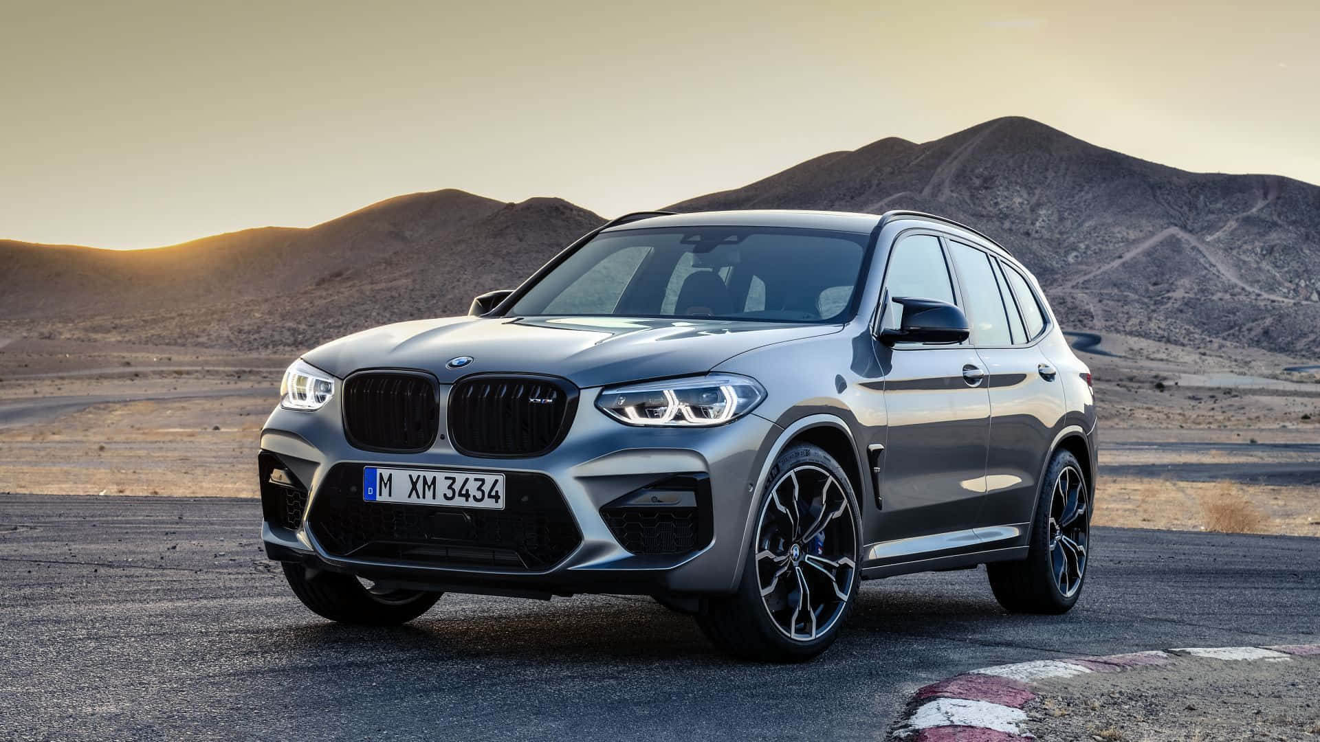 Bmw X3 桌布 壁紙 — 一架時尚的銀色寶馬XM SUV停泊在沙漠賽道上，背景是黃金時段的山脈。