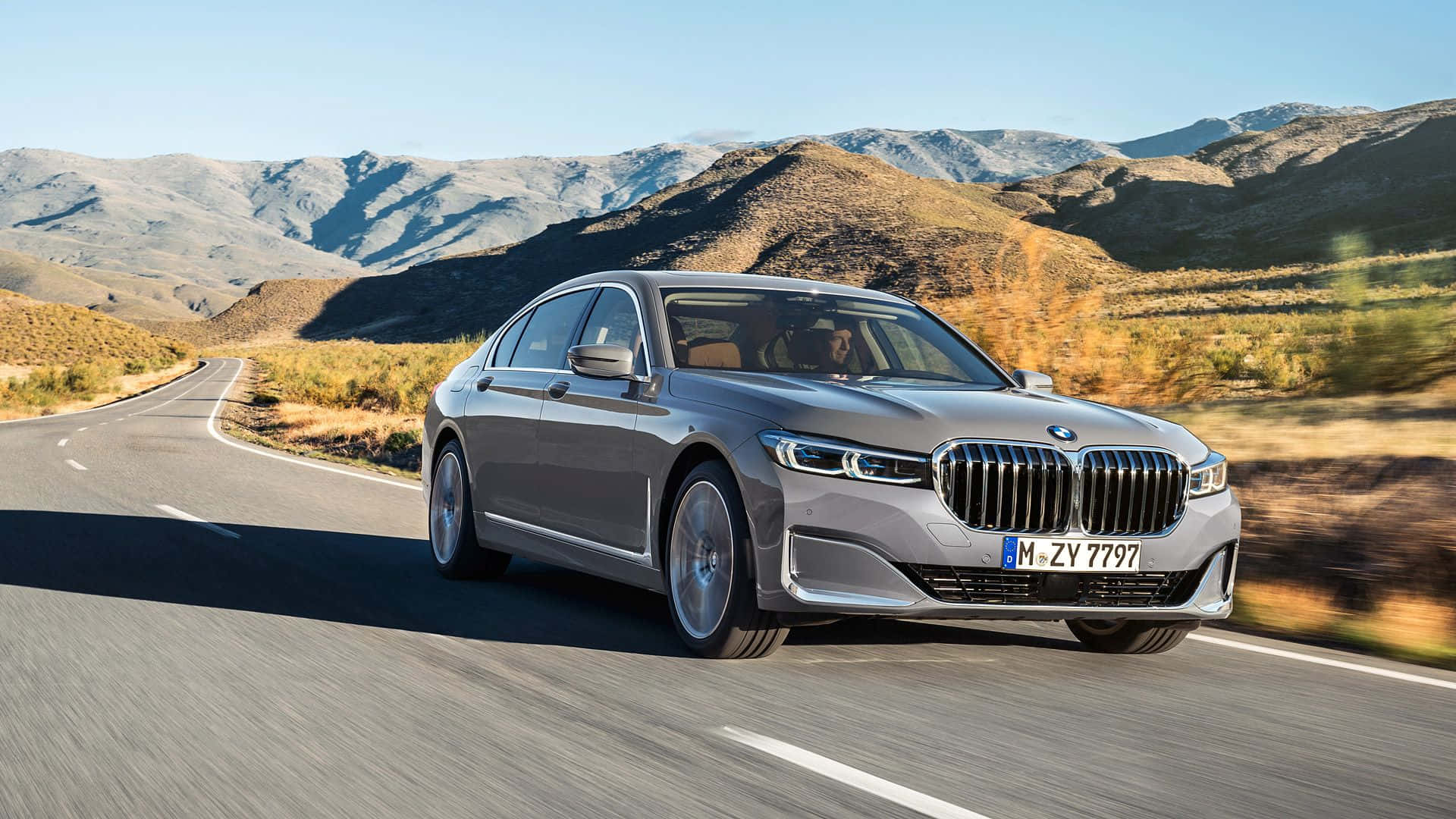 Bmw 7 Series 桌布 壁紙 — 一架時尚的銀色寶馬房車在晴朗藍天下沿著蜿蜒的山路行駛。