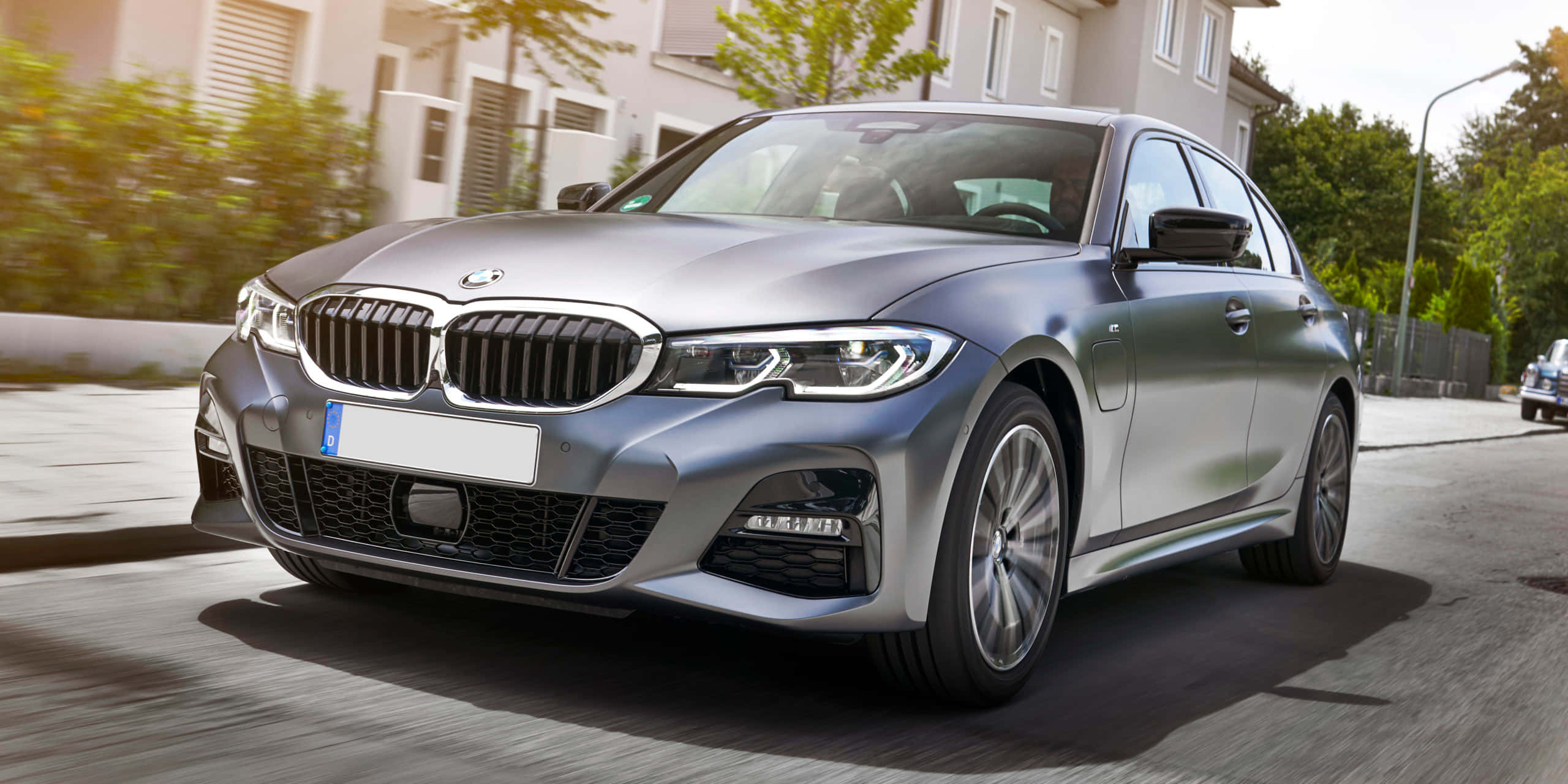 Bmw 3 Series 桌布 壁紙 — 一架時尚的銀色寶馬房車在陽光明媚的住宅街道上滑行，動態模糊強調速度。