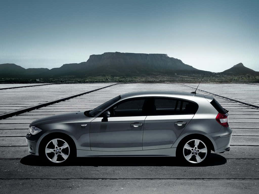 Bmw 1 Series 桌布 壁紙 — 一架時尚的銀色掀背車停泊在木製碼頭上，背景是晴朗天空下的桌山。