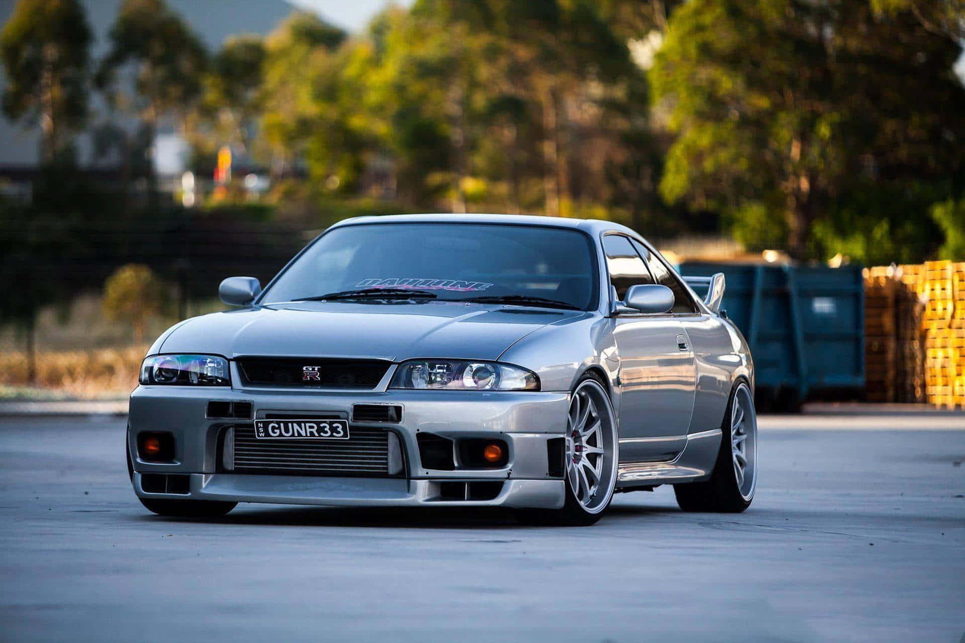 Gtr 桌布 壁紙 — 一架時尚的銀色日產Skyline R34跑車，配備定制輪圈和降低的懸掛系統，在黃金時段停放在混凝土停車場上。