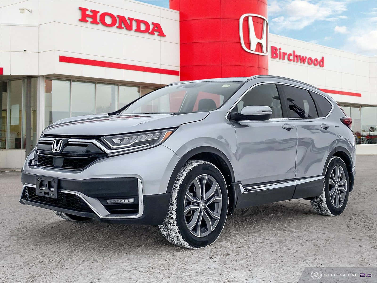 Honda Cr-v 桌布 壁紙 — 一架時尚的銀色本田 CR-V SUV 停泊在現代化的本田經銷店前，店舖採用紅白品牌標誌，背景是清澈的藍天。