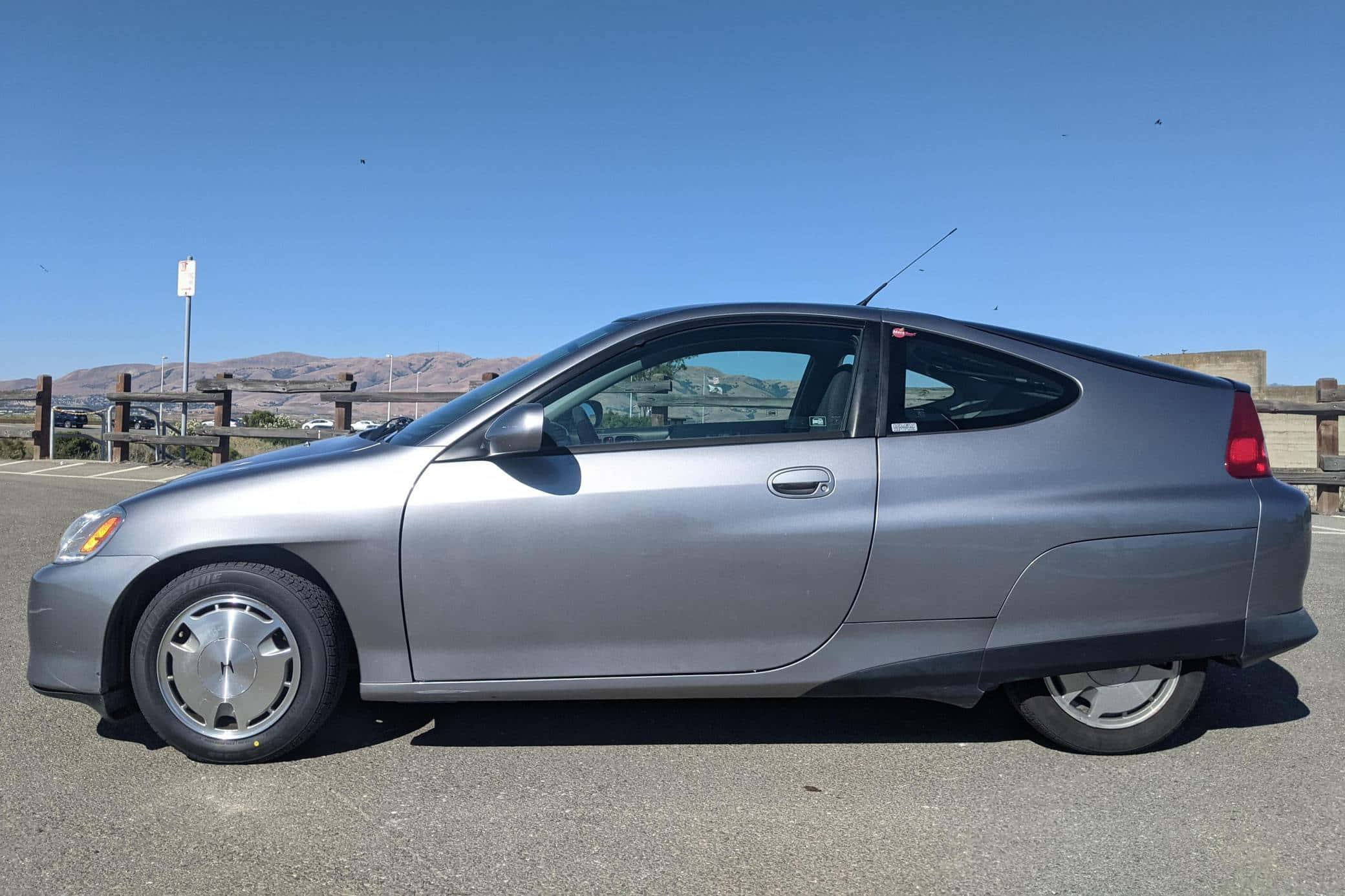 Honda Insight 桌布 壁紙 — 一架時尚的銀色本田Insight混合動力雙門轎跑車停泊在陽光明媚的停車場，遠處有山丘，天空清澈湛藍。