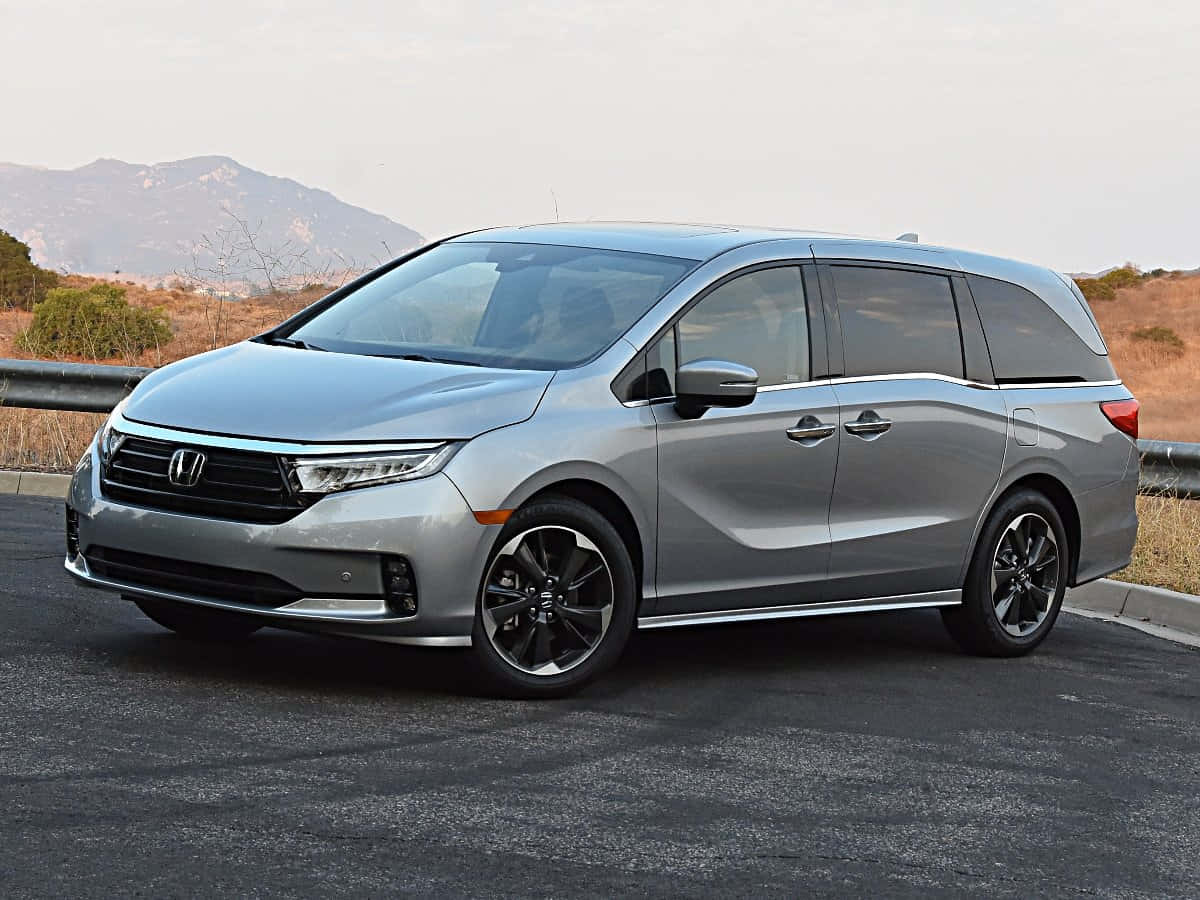Honda Odyssey 桌布 壁紙 — 一架時尚的銀色本田奧德賽小型貨車停泊在瀝青路上，背景有山脈和乾燥灌木。